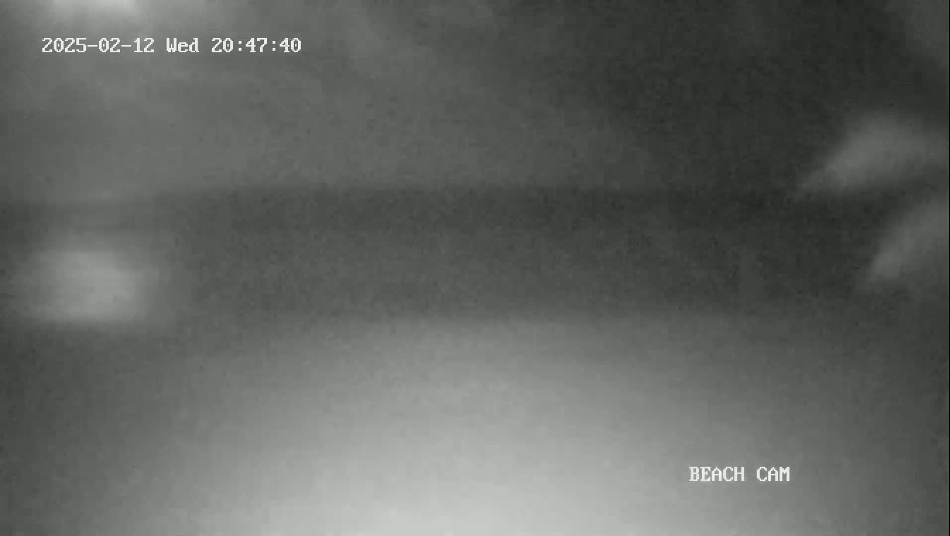 A grainy, nighttime beach cam image shows a dark, overcast sky and a dimly lit beach.