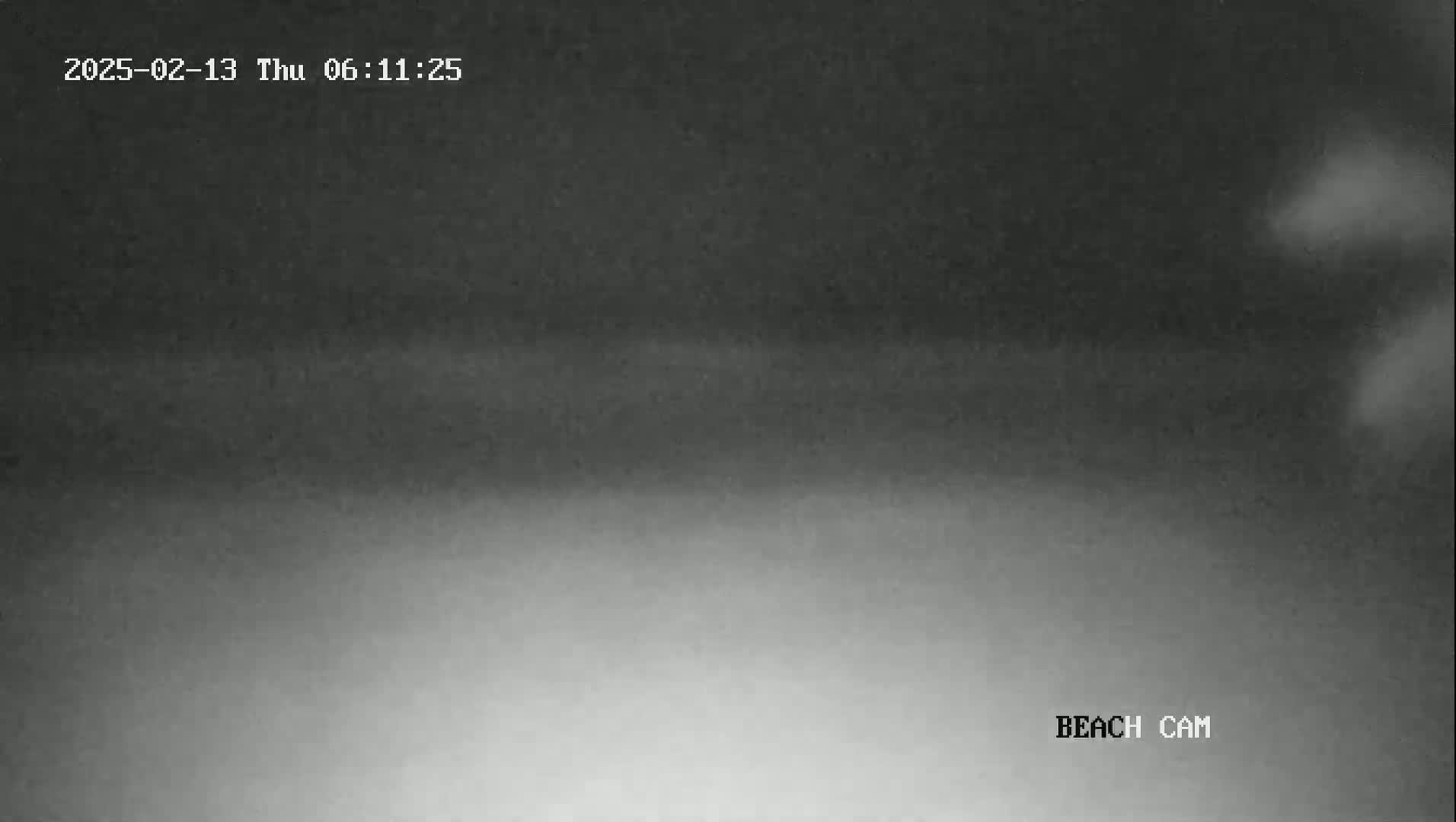 A dark, nighttime beach scene is shown, with a faint, lighter horizon line visible.