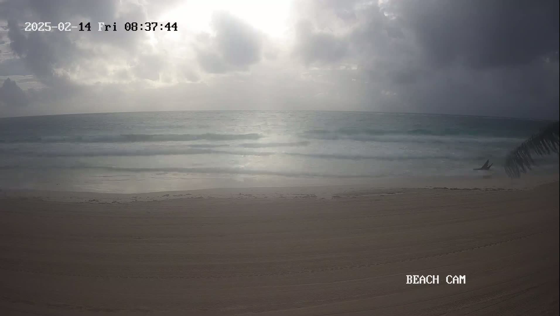 A mostly cloudy sunrise illuminates a wide sandy beach and gently rolling ocean waves.
