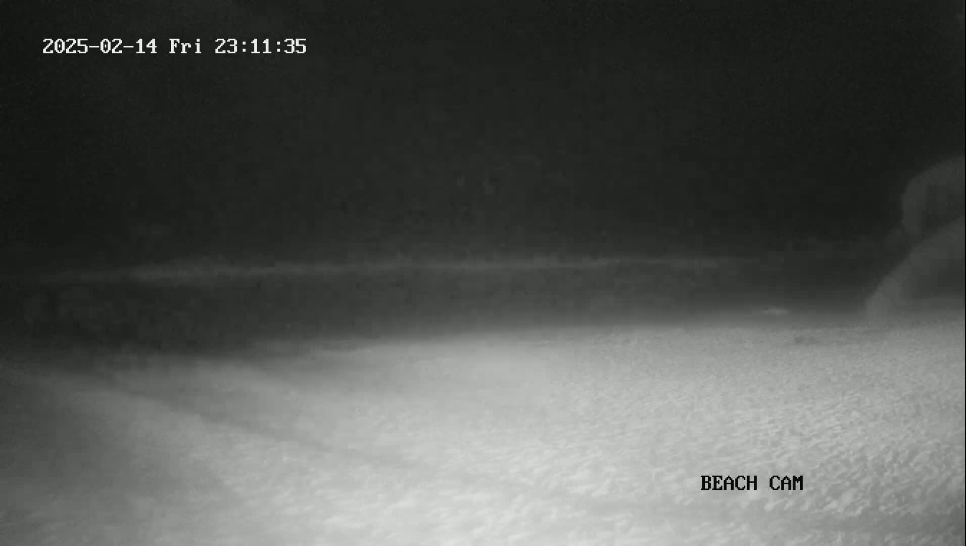 A nighttime, low-light beach scene shows a dark sandy expanse under a mostly clear sky.