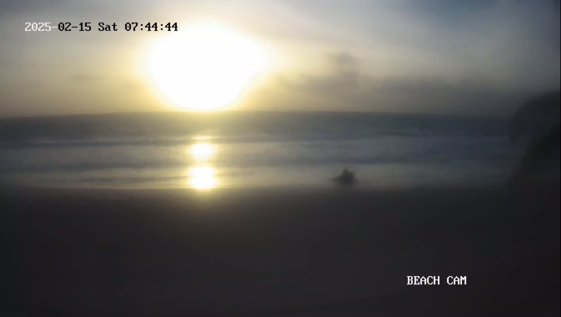 A hazy sunrise over a calm ocean beach.