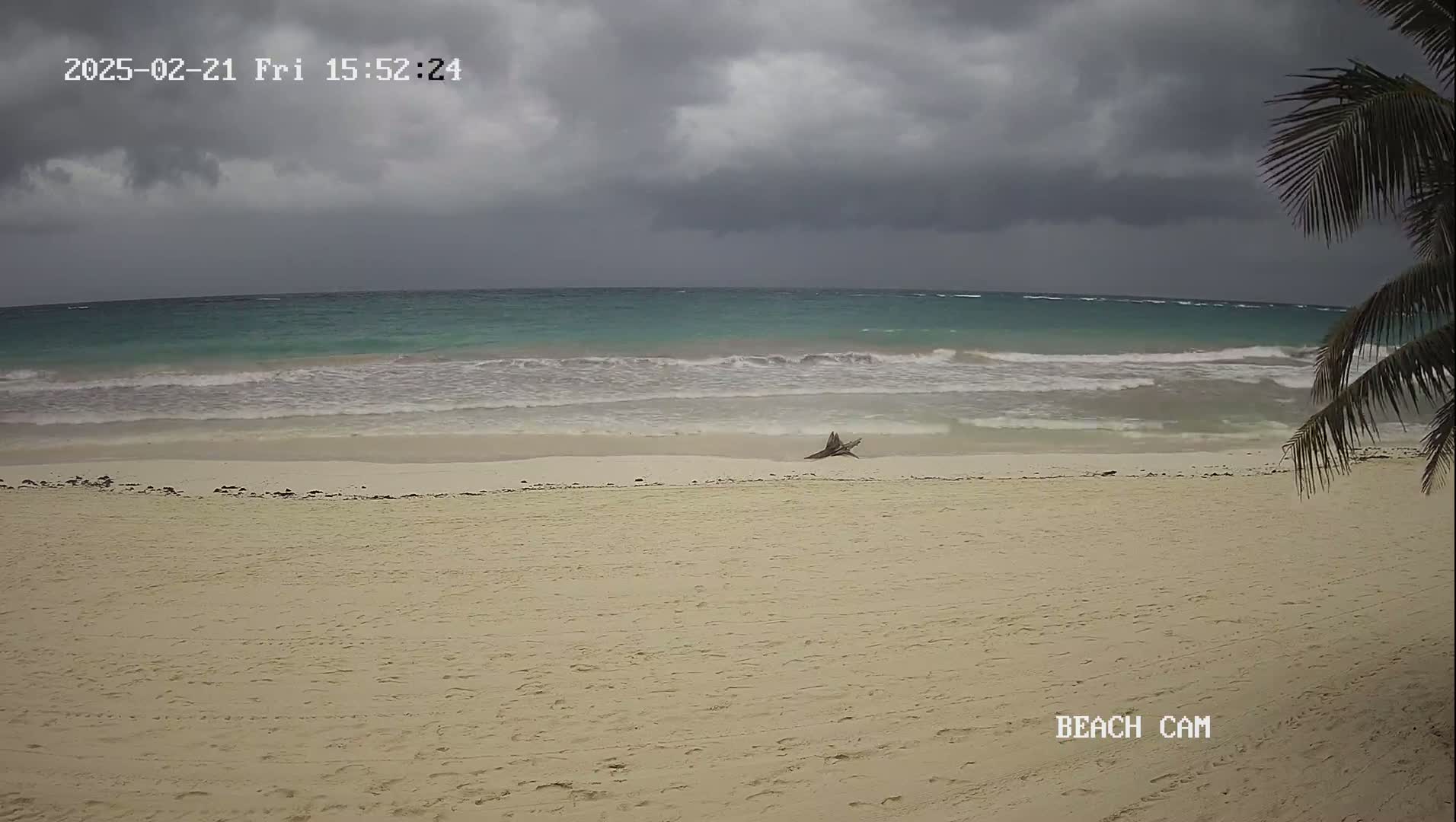 A sandy beach with a partly cloudy, overcast sky and turquoise waves rolls onto the shore.
