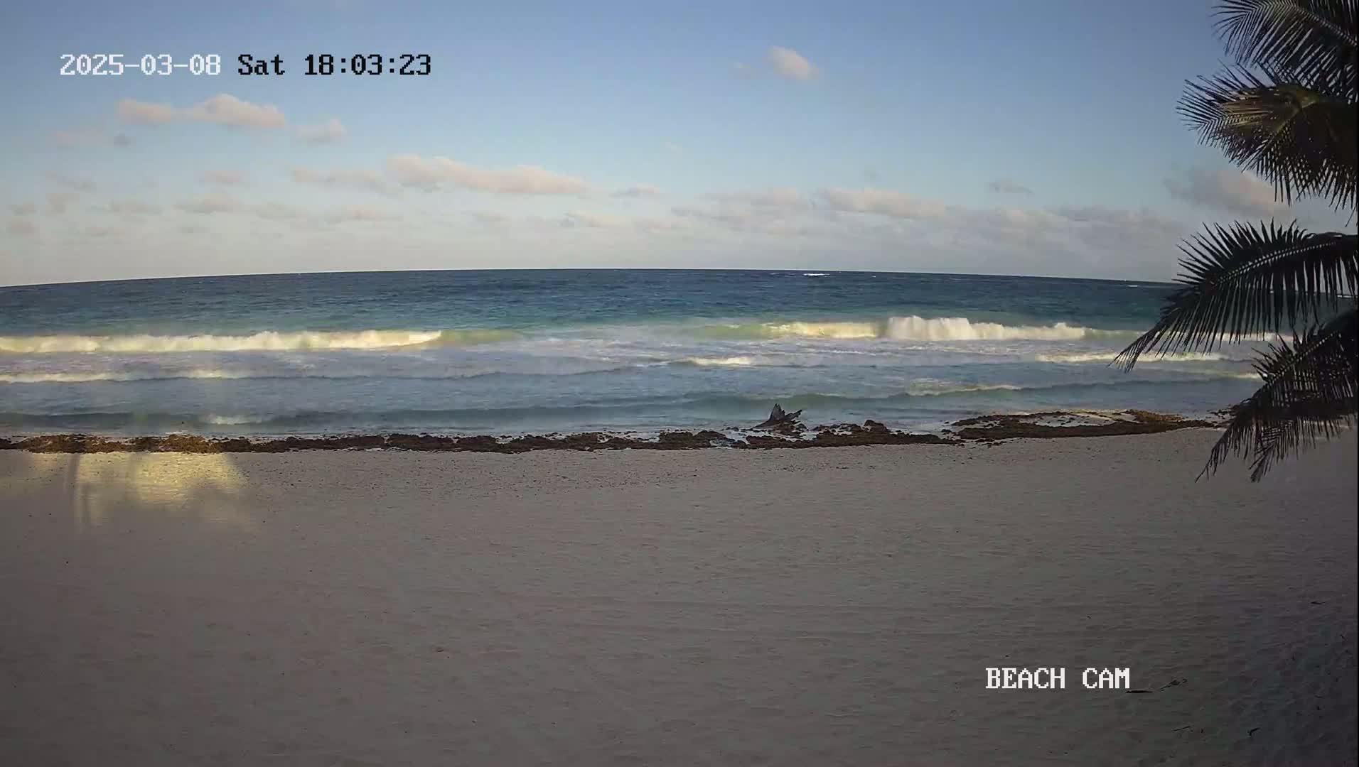 A sandy beach with small waves rolling onto the shore under a partly cloudy sky.