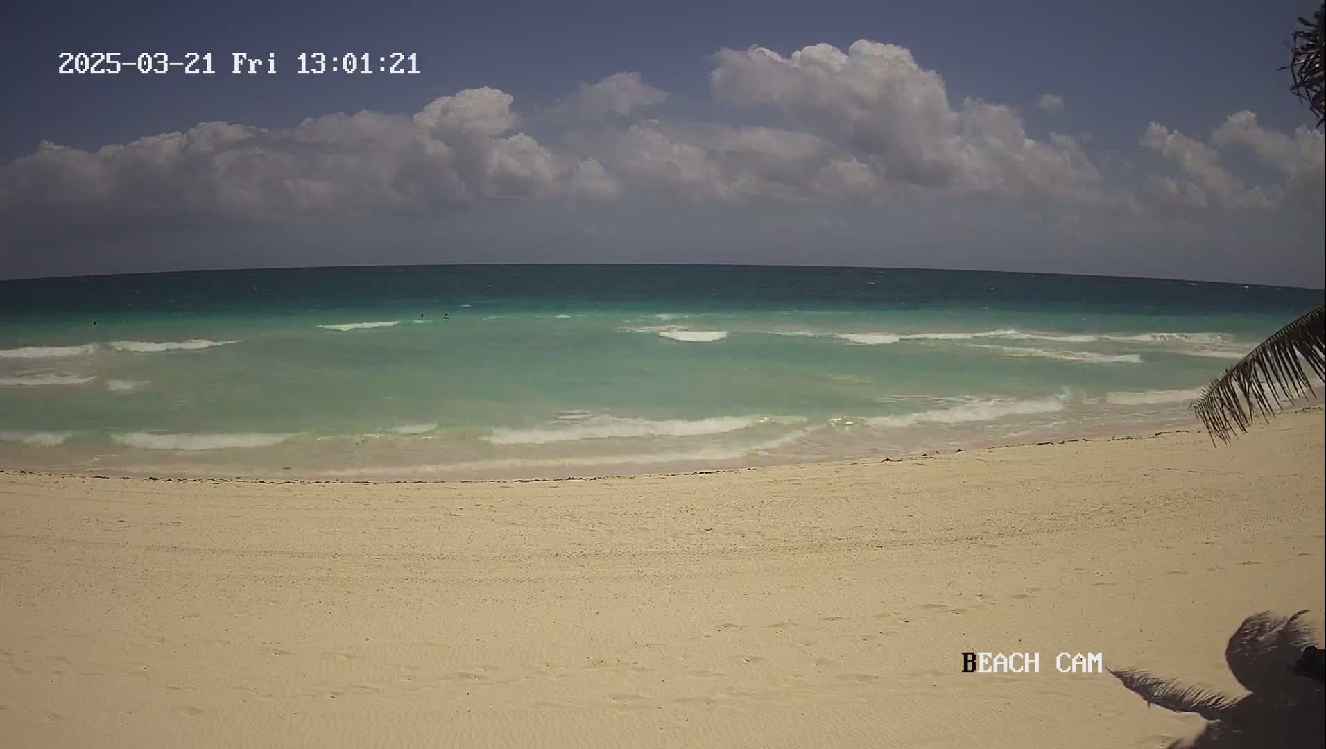 A sandy beach with light-colored sand and a turquoise ocean with small waves under a partly cloudy sky.
