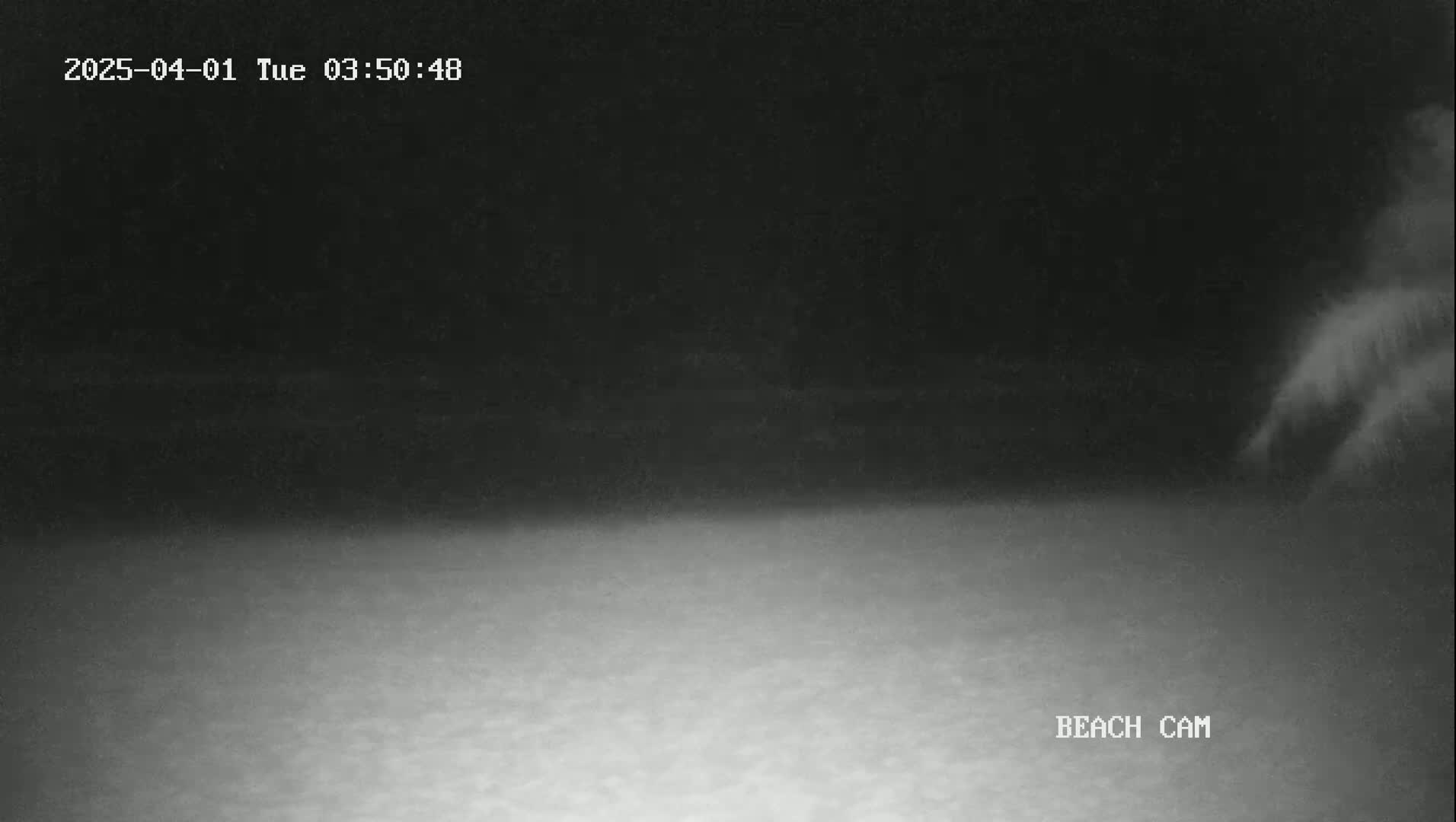 A low-light nighttime beach scene shows a dark sky and a lighter-colored beach with indistinct features.