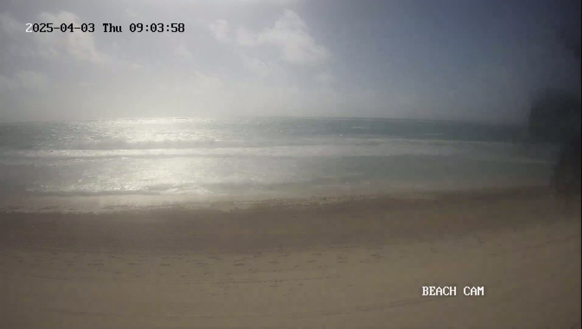 A sandy beach with small waves and a partly sunny sky is visible.