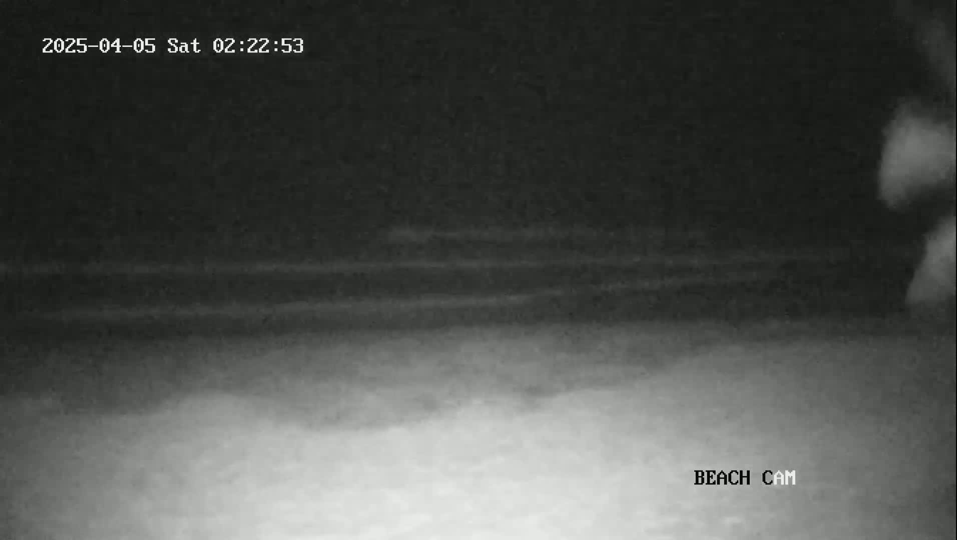 A nighttime beach scene shows a dark, possibly cloudy sky above a light-colored sandy beach.