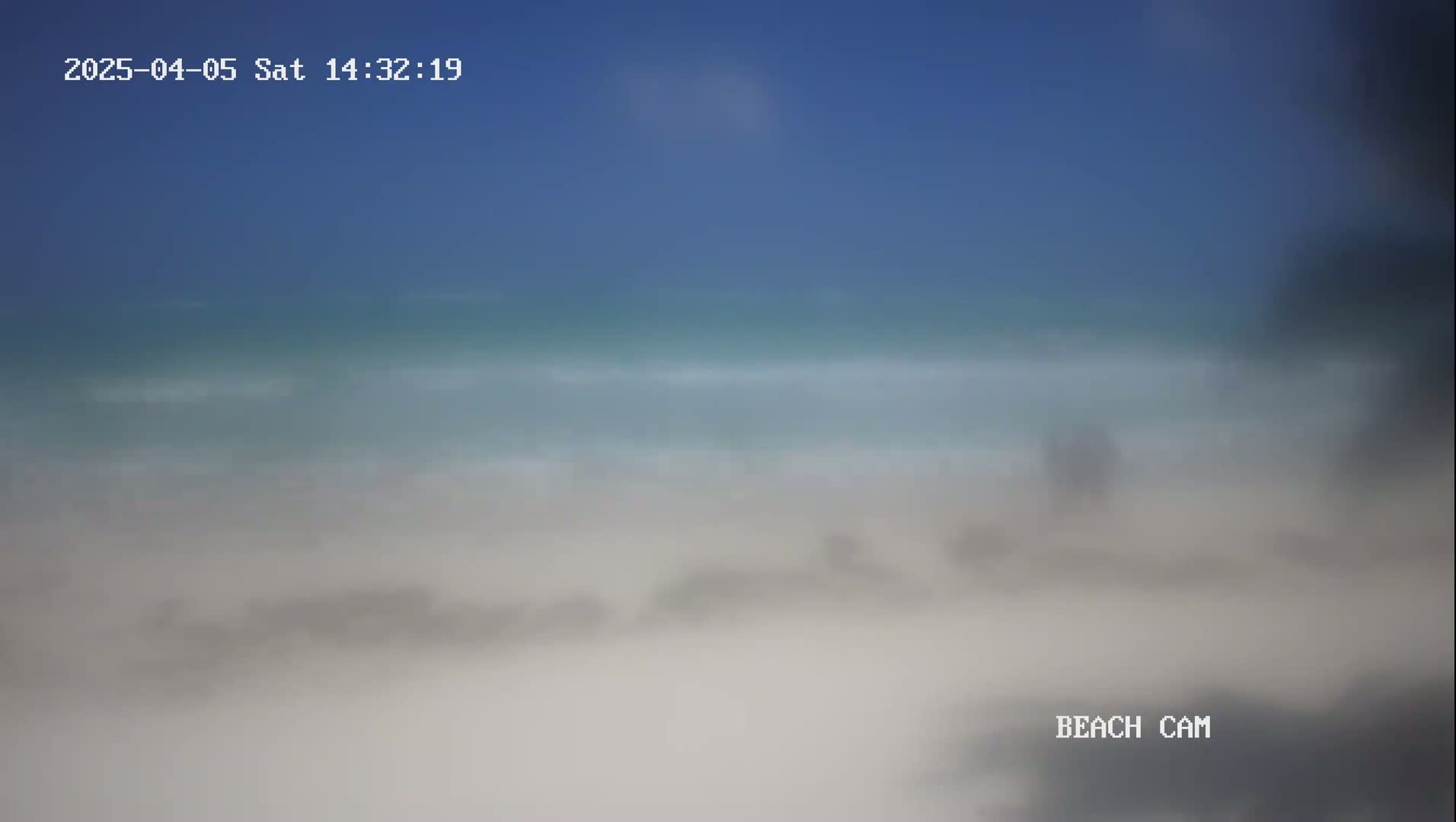 A blurry image shows a beach scene on a clear, sunny day with light waves lapping the shore.
