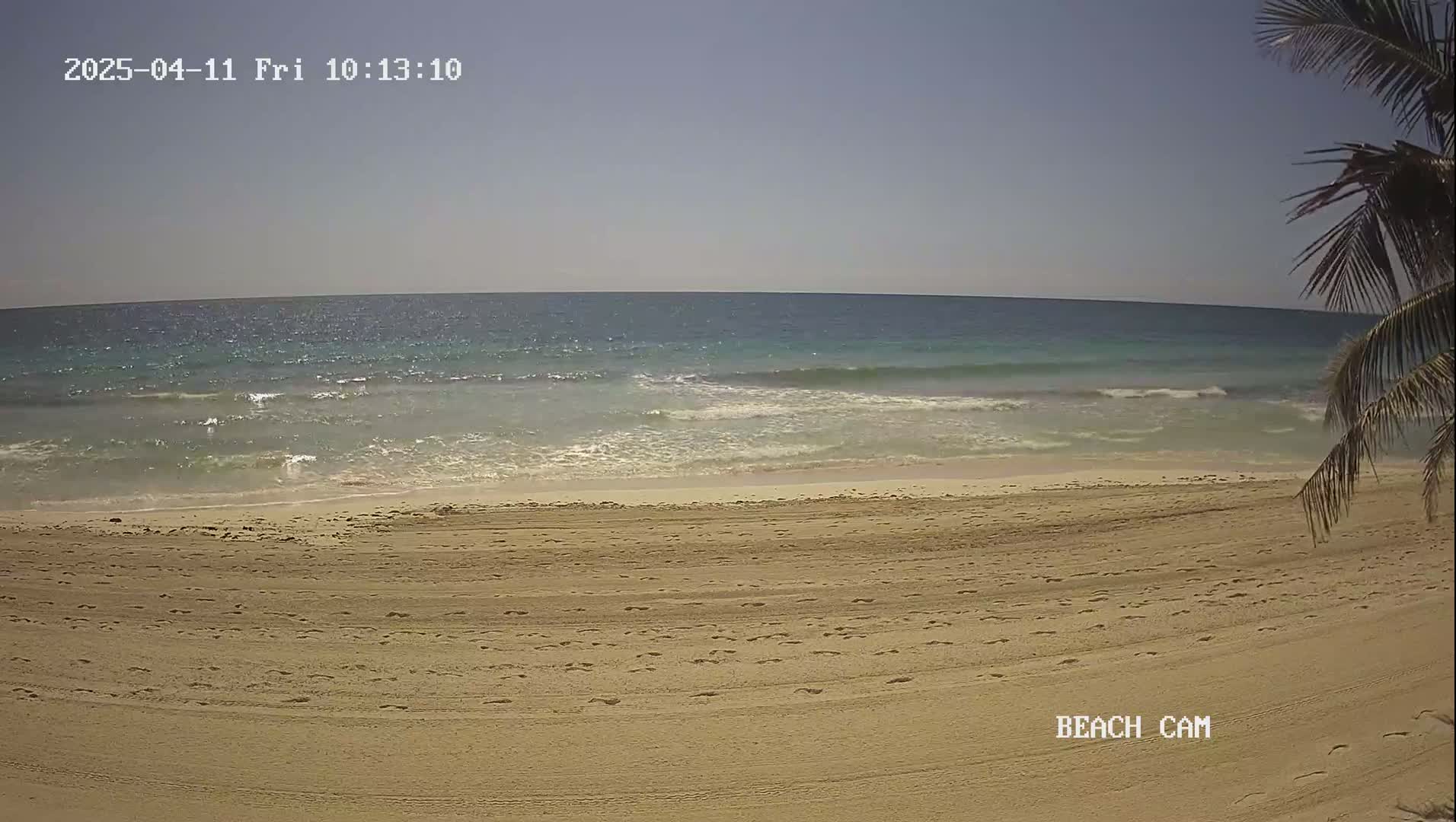 A sandy beach with footprints and a calm ocean under a clear sky is shown.