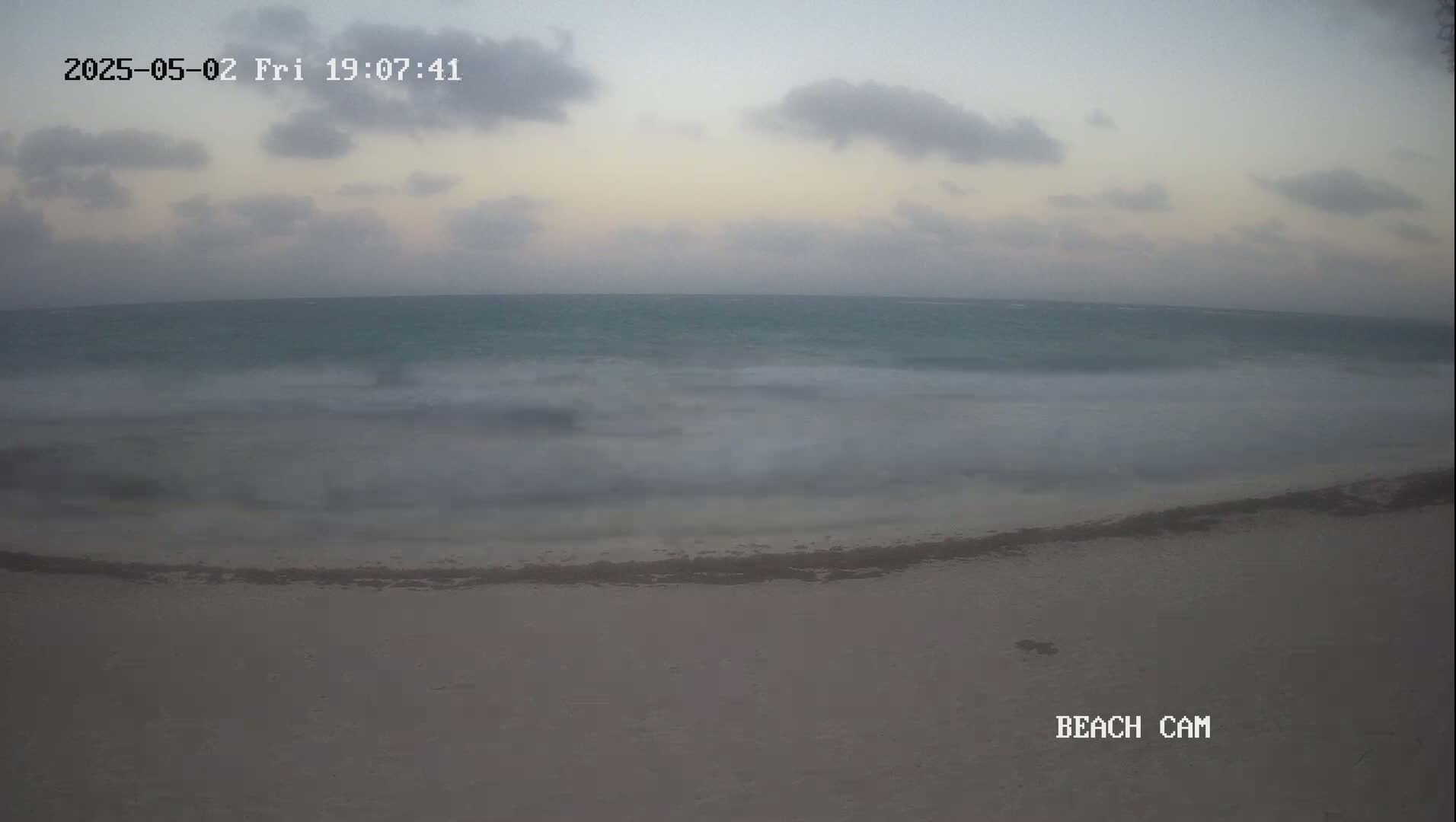 A sandy beach meets a somewhat choppy ocean under a cloudy, dusky sky.