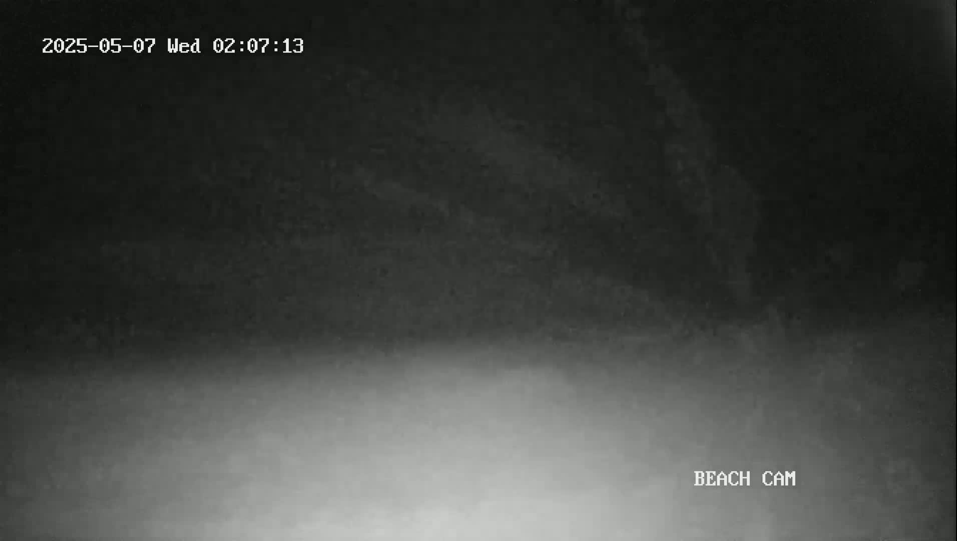 A low-light nighttime image shows a dark, hazy or foggy beach.