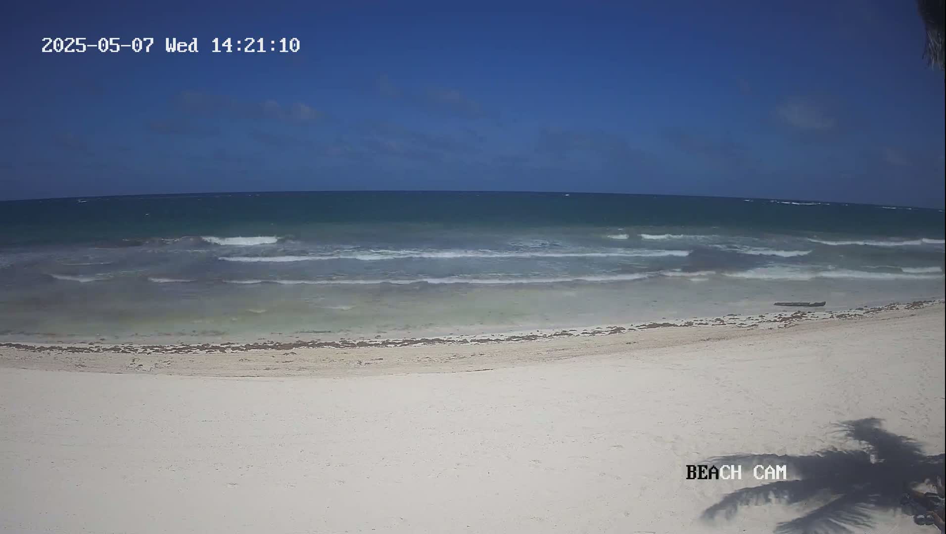A mostly clear sky overlooks a white sandy beach with small waves lapping the shore.