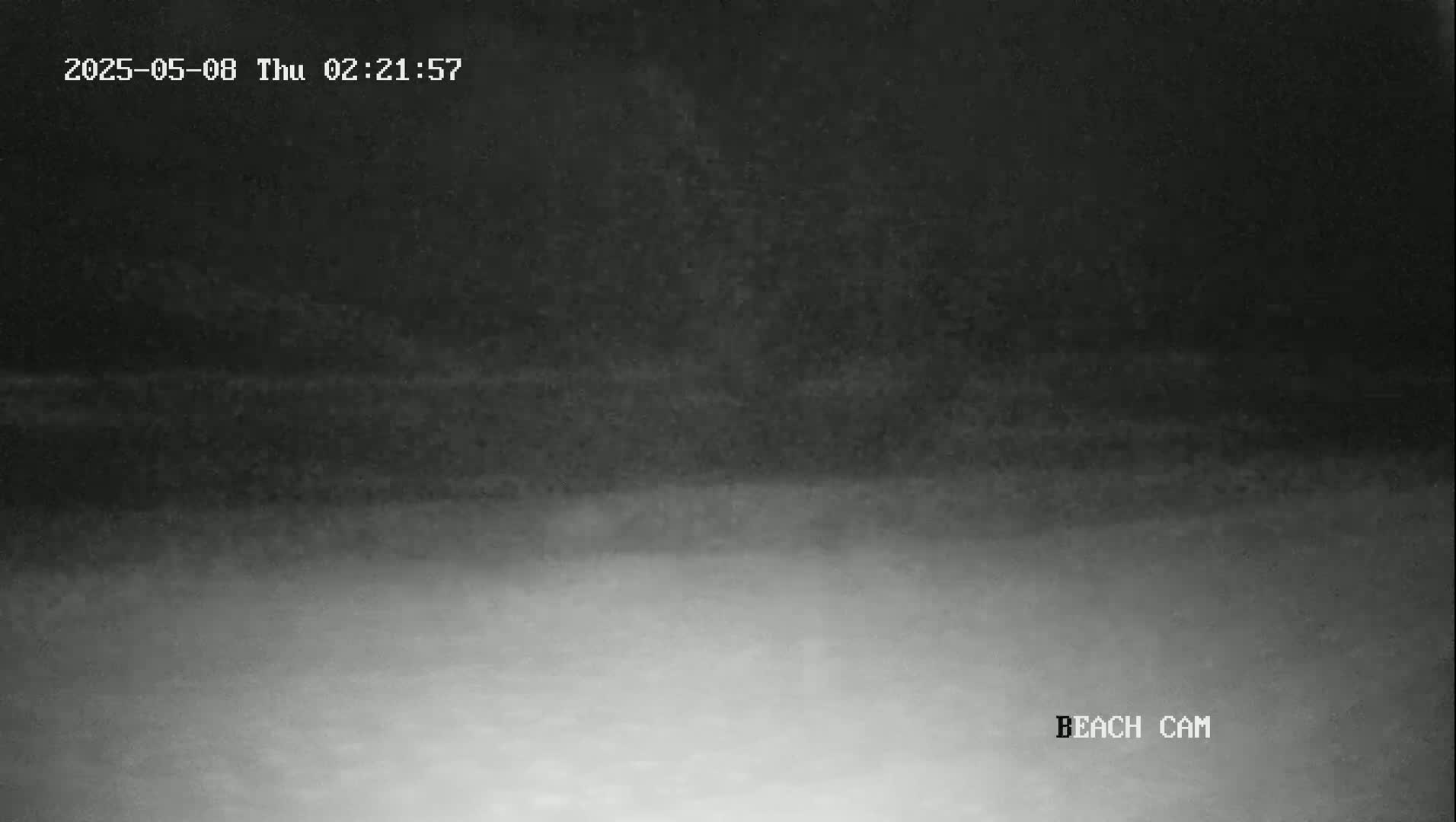 A low-light nighttime image shows a dark beach under a dark sky.