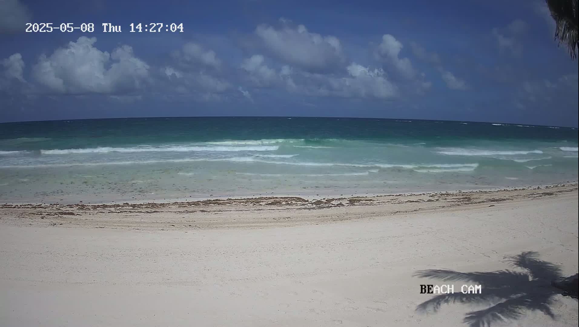 A partly cloudy day shows a wide expanse of light teal ocean waves lapping a white sand beach.