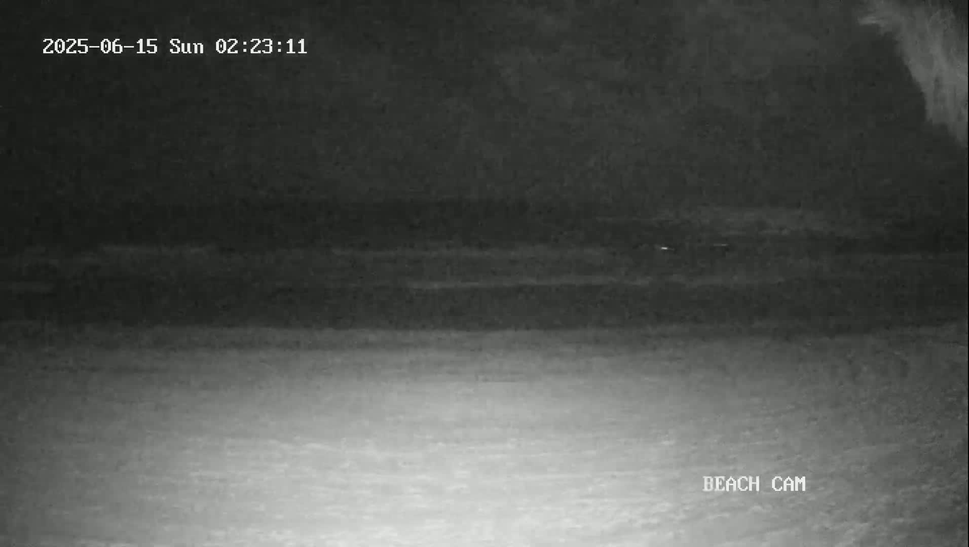A nighttime beach scene is shown, with dark water and a light-colored sandy beach visible under low-light conditions.