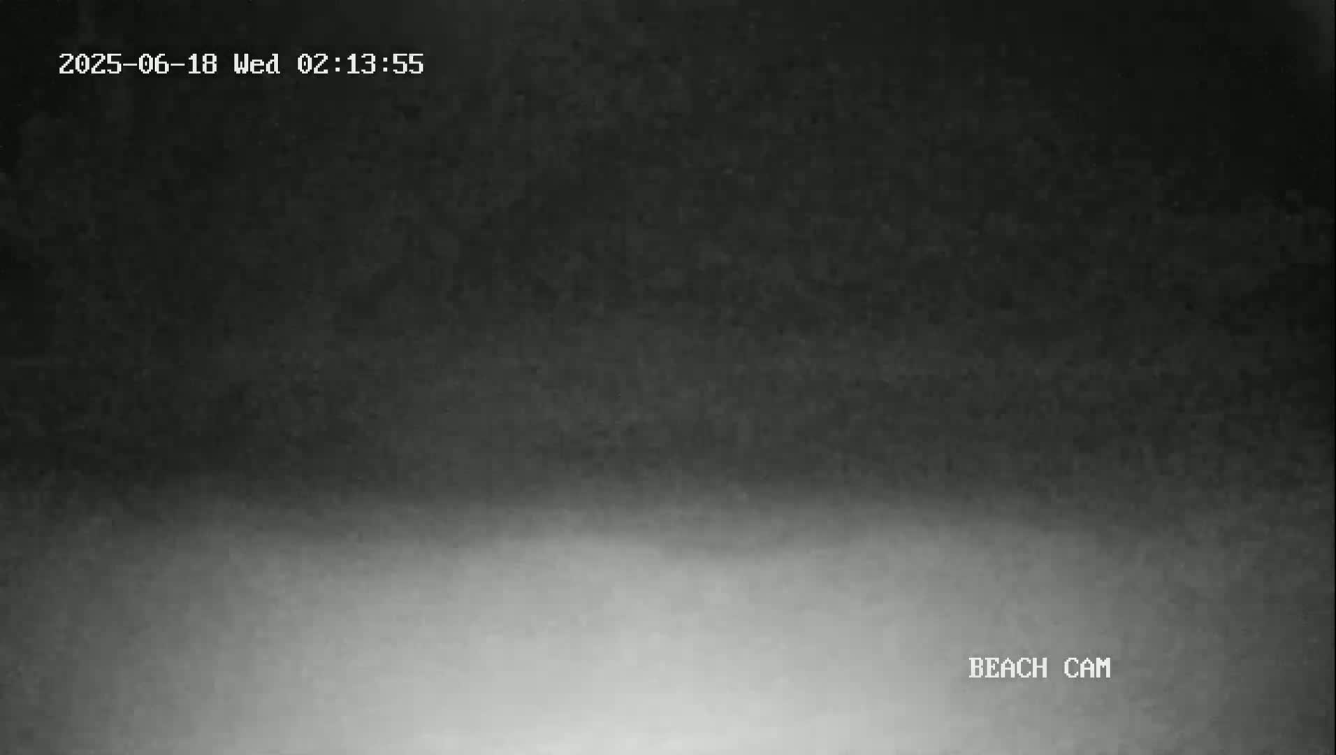 A dark, blurry image shows a mostly dark sky transitioning to a lighter gray at the bottom, suggesting a nighttime or pre-dawn beach scene with fog or mist.