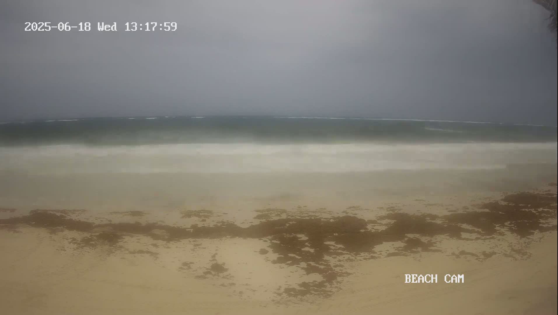 A sandy beach with dark patches is shown under an overcast sky, with choppy waves visible in the distance.