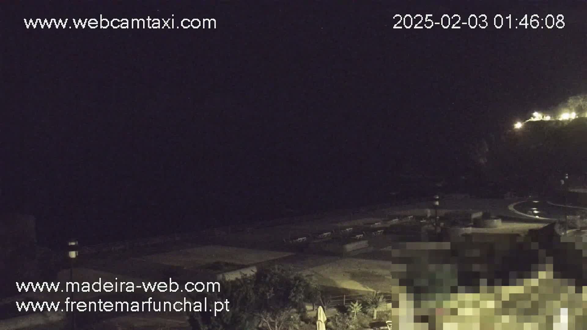 A nighttime view of a dark beach with some lights visible in the distance, under a clear, dark sky.