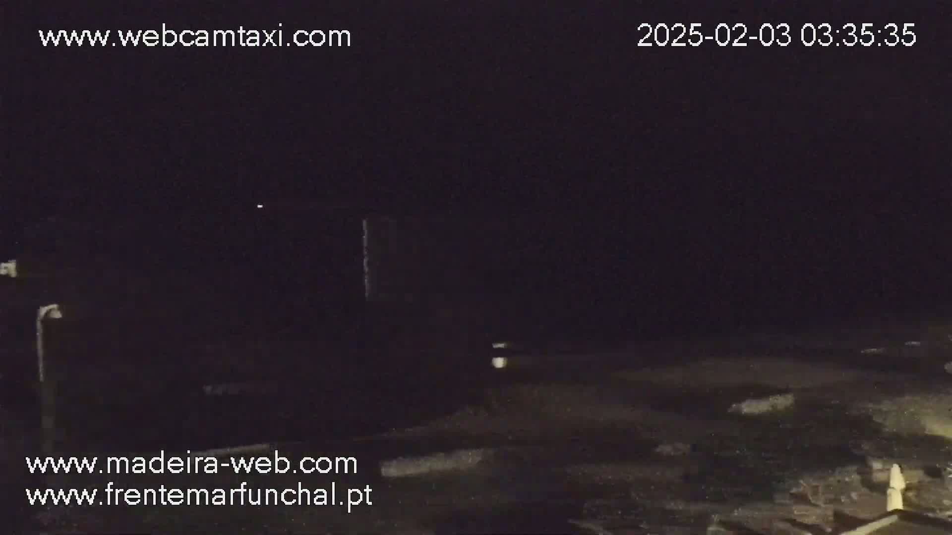 A dark, nighttime outdoor scene shows a mostly empty area with a faint light source in the distance.