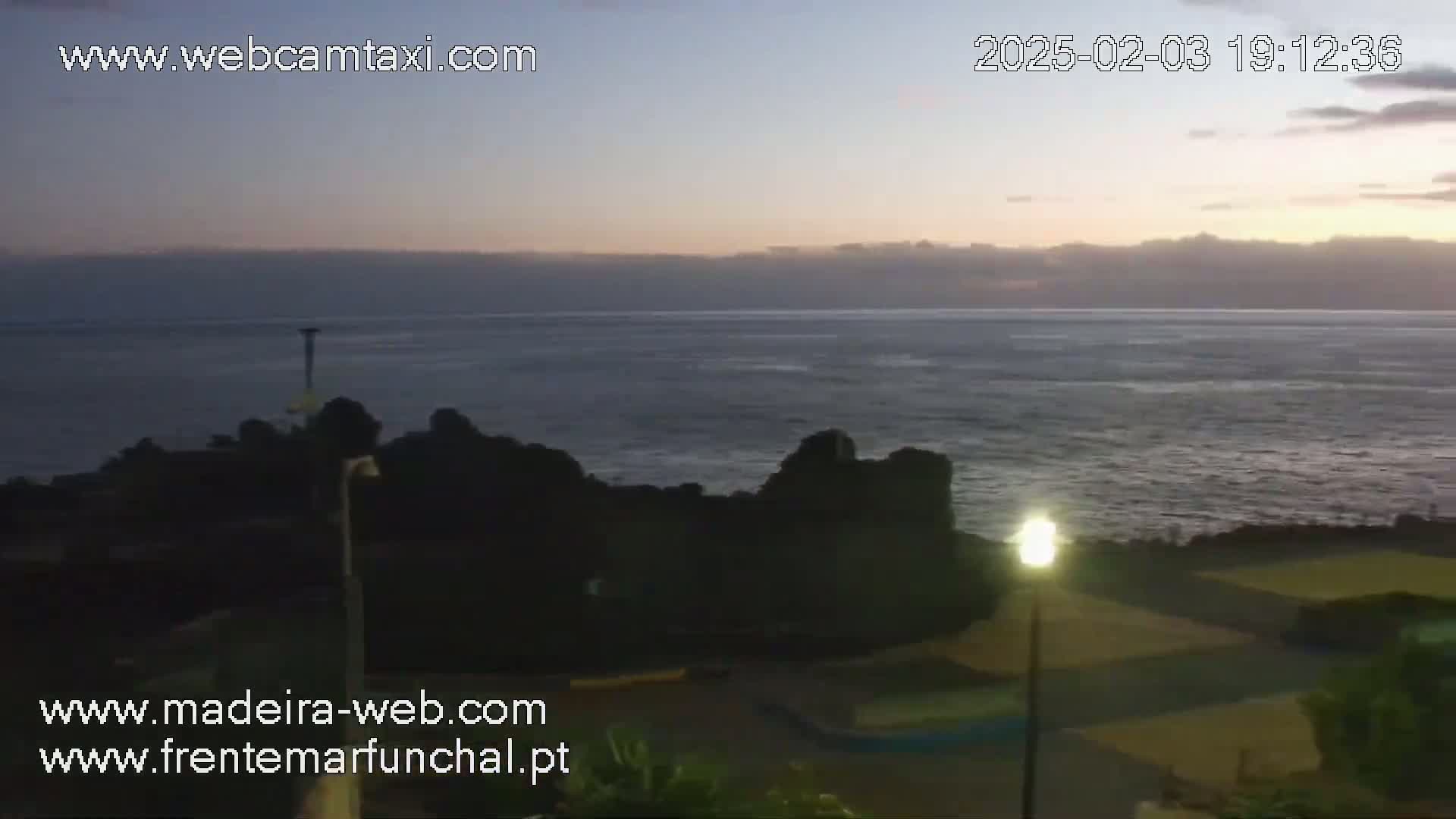 A twilight view shows a dark, rocky coastline meeting a calm ocean under a mostly clear sky.