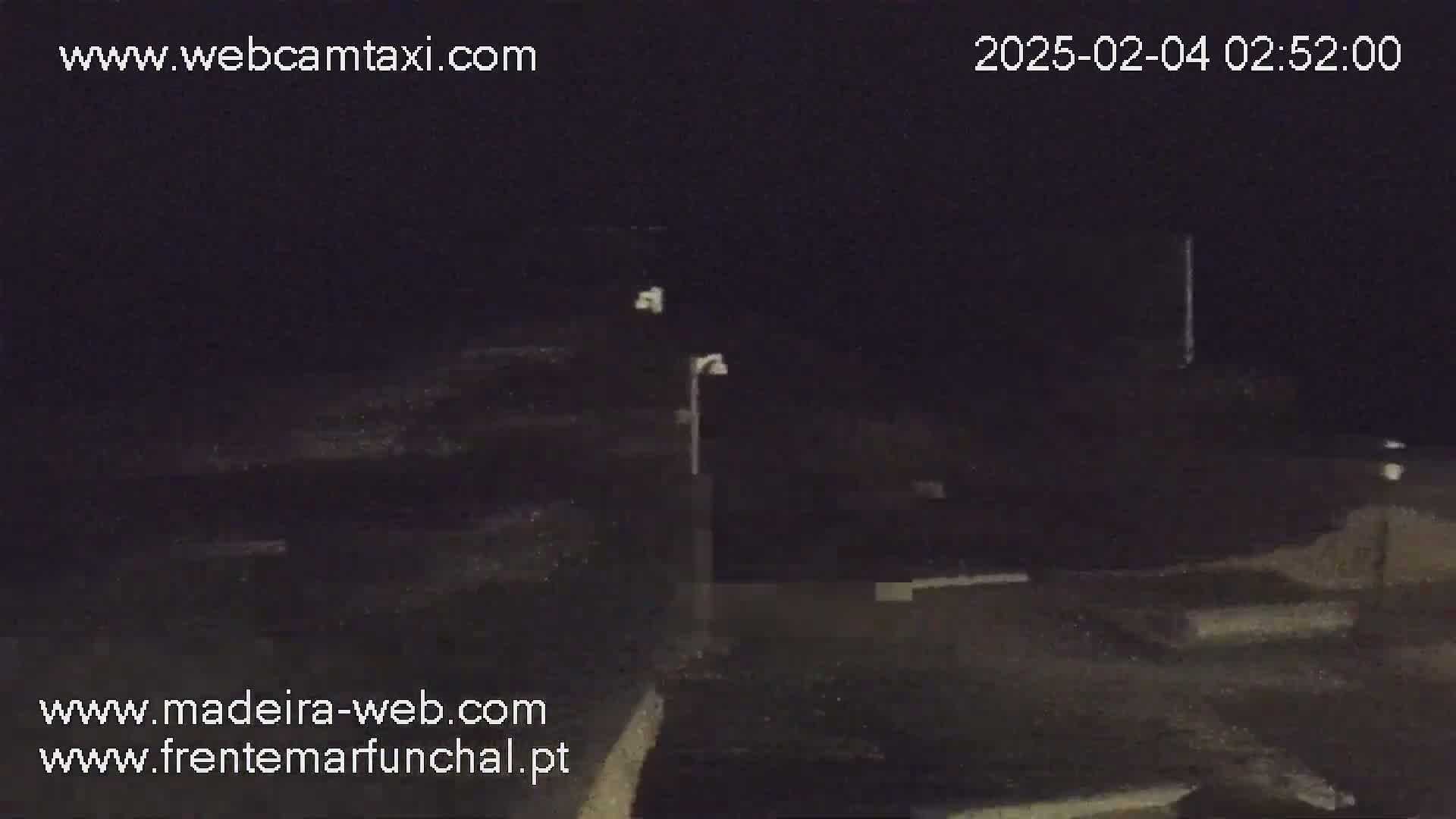 A nighttime, low-light view shows a dark, seemingly empty area with a single lamppost, possibly a parking lot or waterfront.