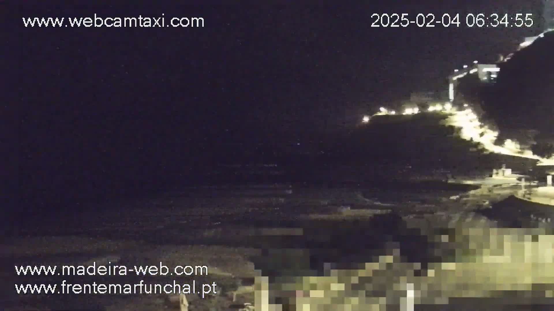 A nighttime, seaside view shows dark, wavy water and a cliffside illuminated with lights.