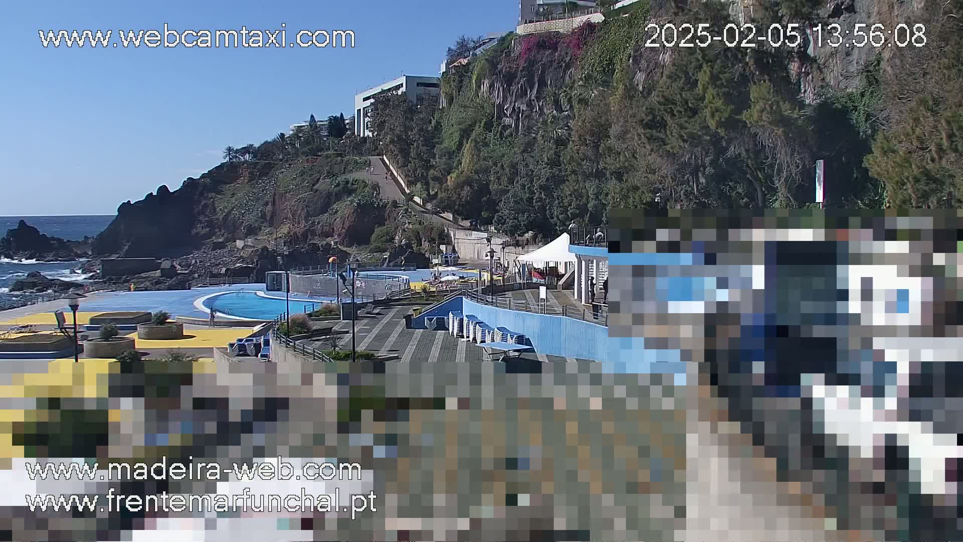 An outdoor oceanside pool area with a clear blue sky and a rocky cliff in the background.