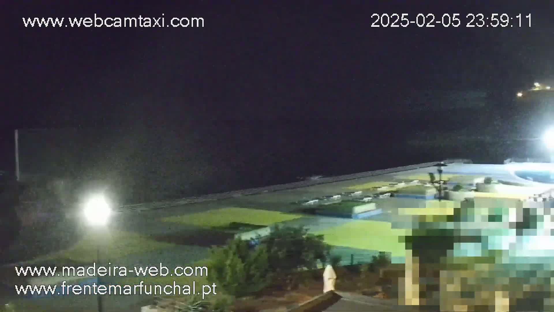 A nighttime view of a coastal area with a paved walkway, buildings, and some vegetation under a dark sky.