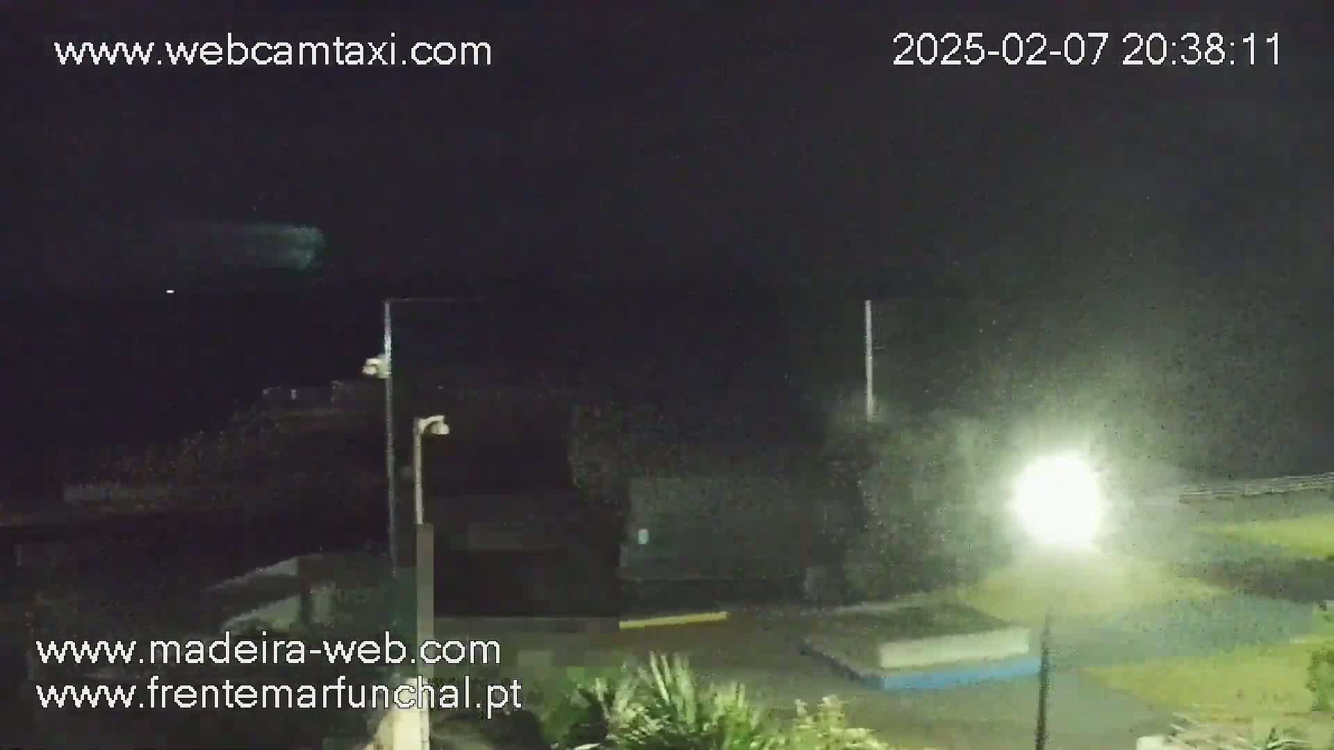 A nighttime outdoor scene shows rain falling on a dark parking lot illuminated by a bright lamppost.