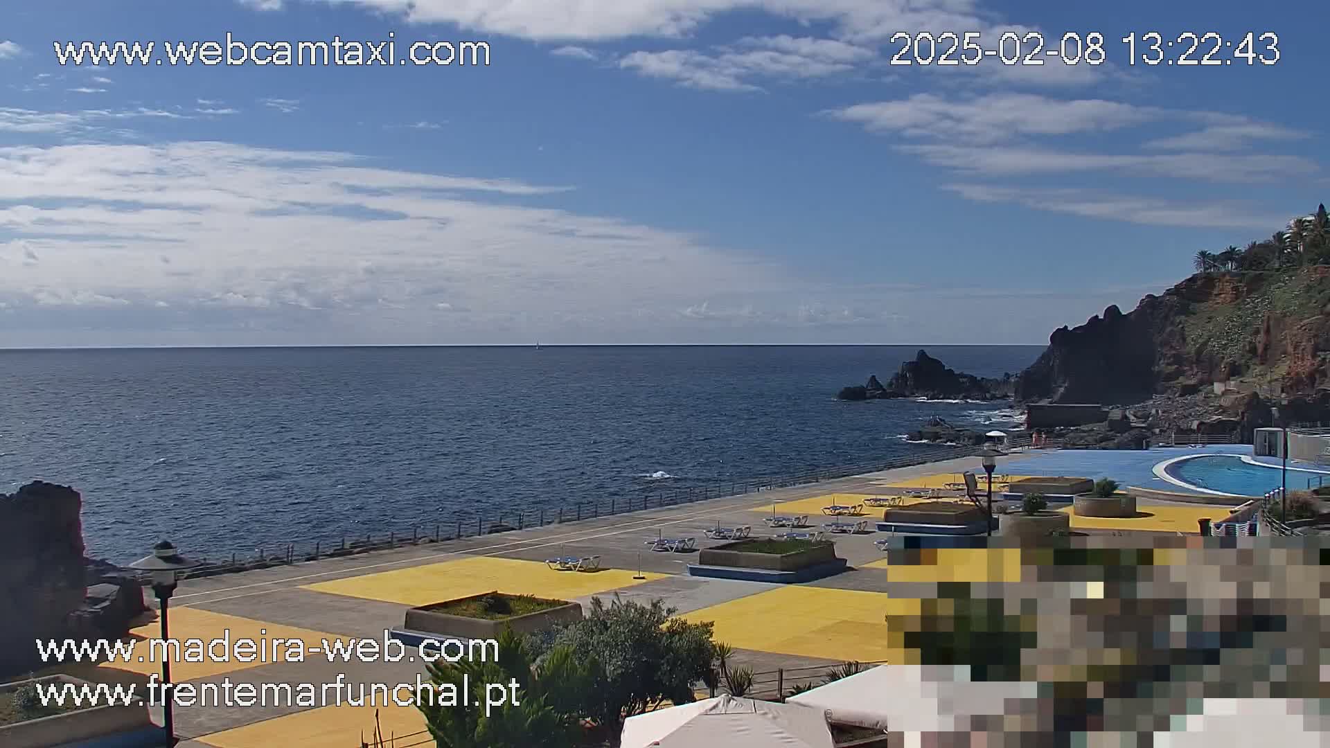 An outdoor view of a seaside area with a swimming pool and surrounding deck chairs, under a partly cloudy sky.
