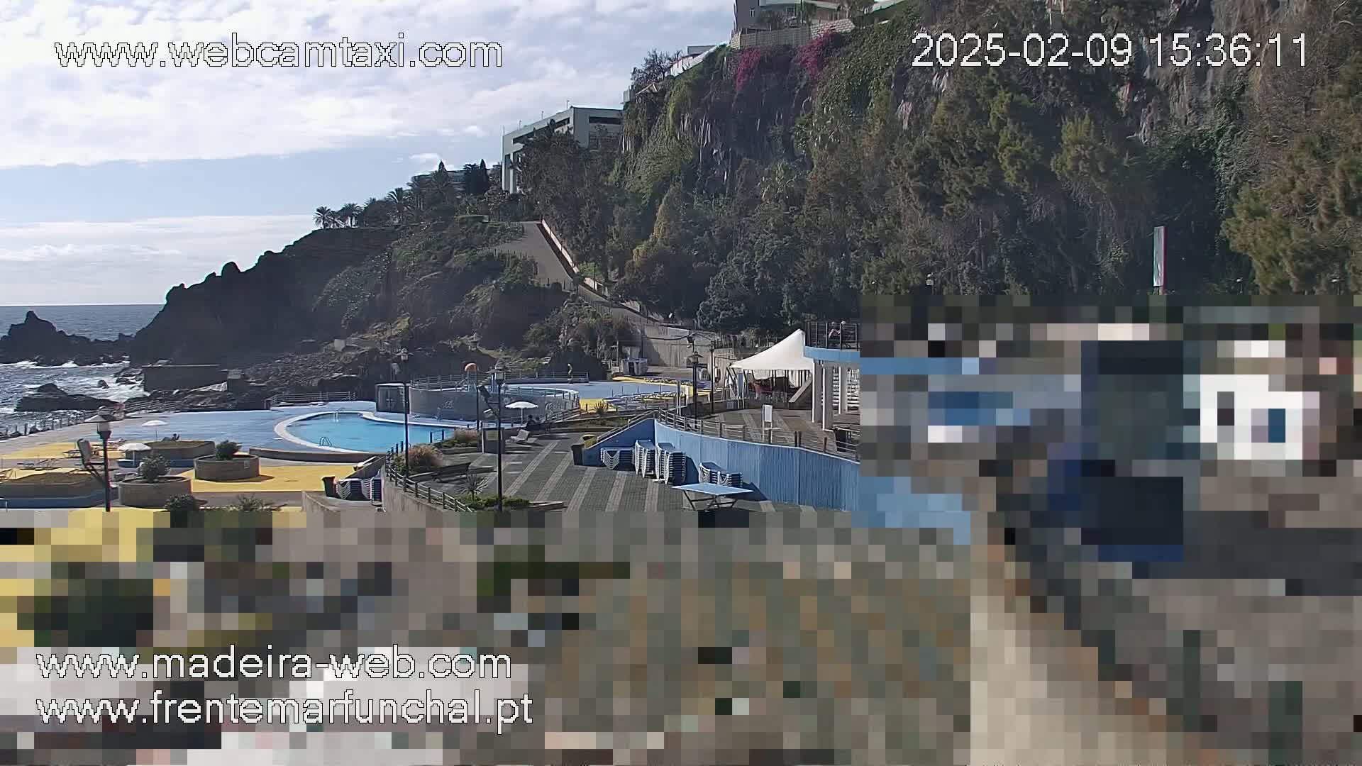 An outdoor view of a seaside pool area with a partially cloudy sky, situated on a cliffside next to a rocky ocean shore.