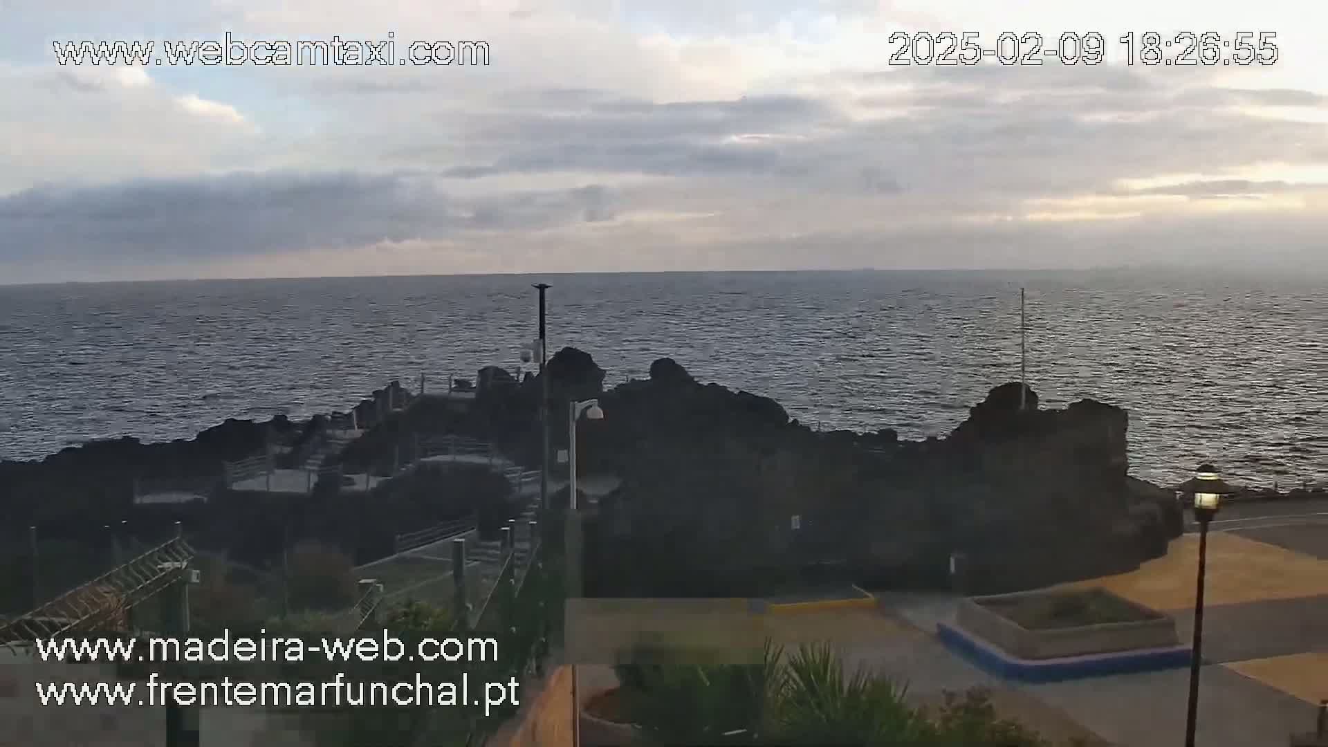 A rocky coastline meets a calm, overcast ocean under a cloudy sky.