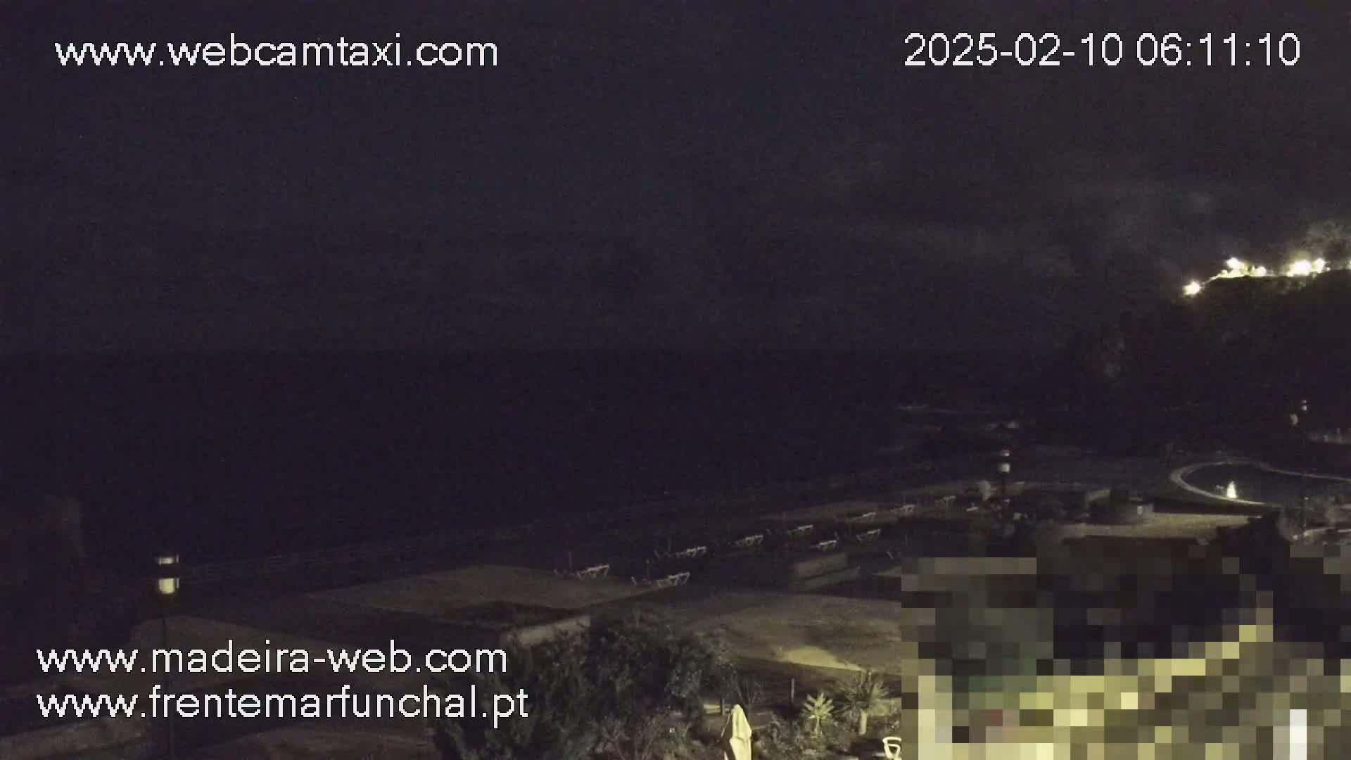 A nighttime view overlooking a dark ocean, a pool, and outdoor furniture, under a mostly cloudy sky.