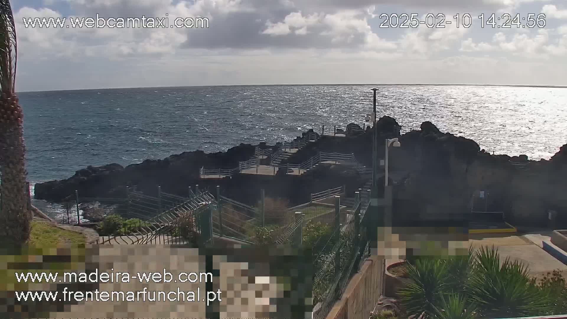A partly cloudy day shows a rocky coastline with stairs leading down to the ocean, which has a slightly choppy surface.