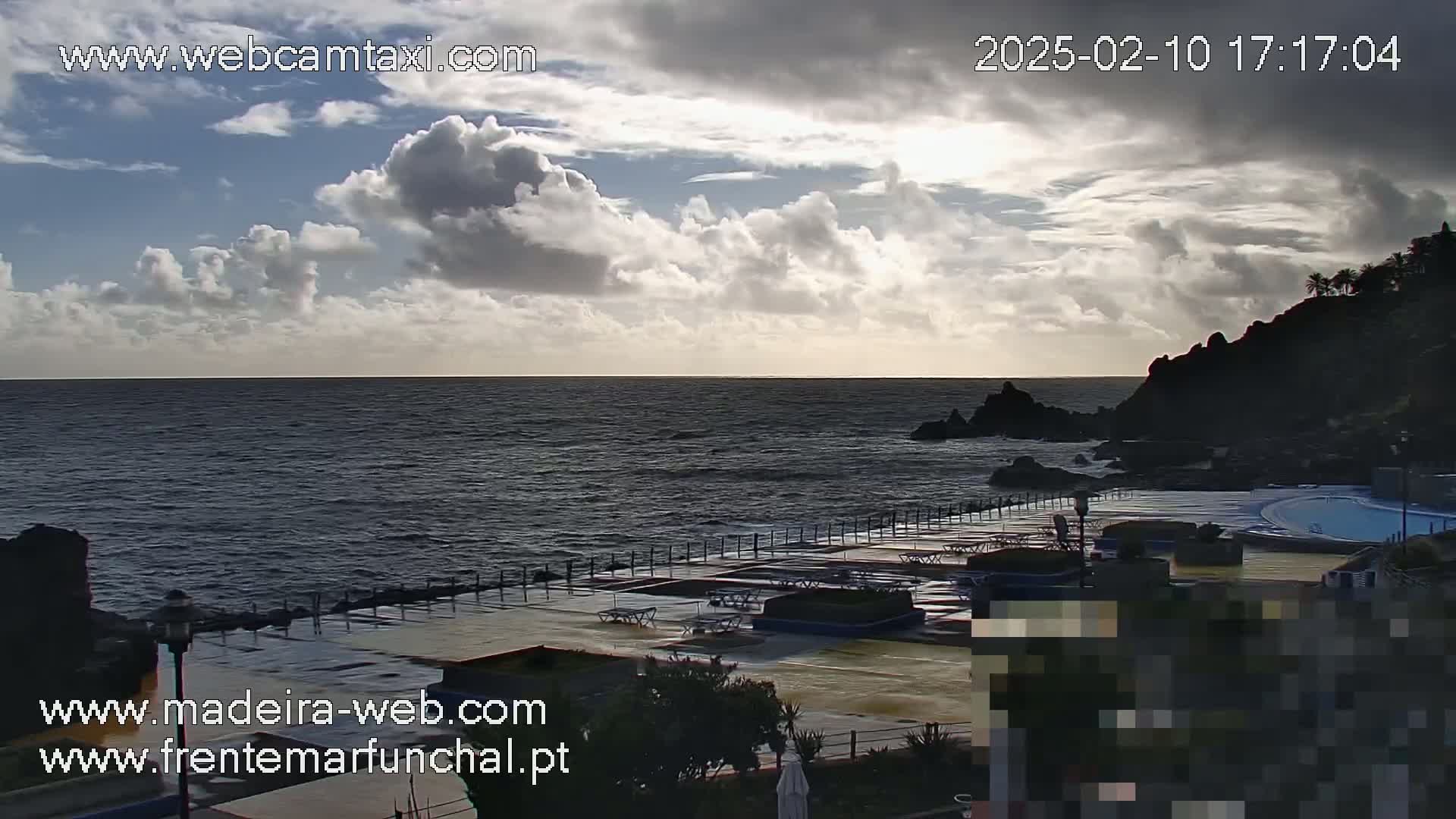 A partly cloudy sky overlooks a dark ocean, rocky coastline, and an outdoor swimming pool area.