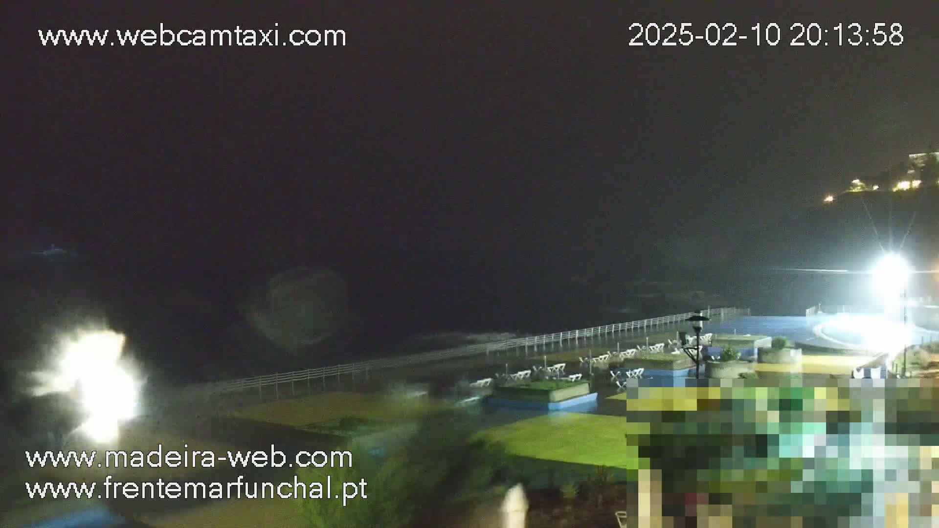 A nighttime coastal scene shows crashing waves against a seawall near an outdoor patio area under dark, possibly stormy, conditions.