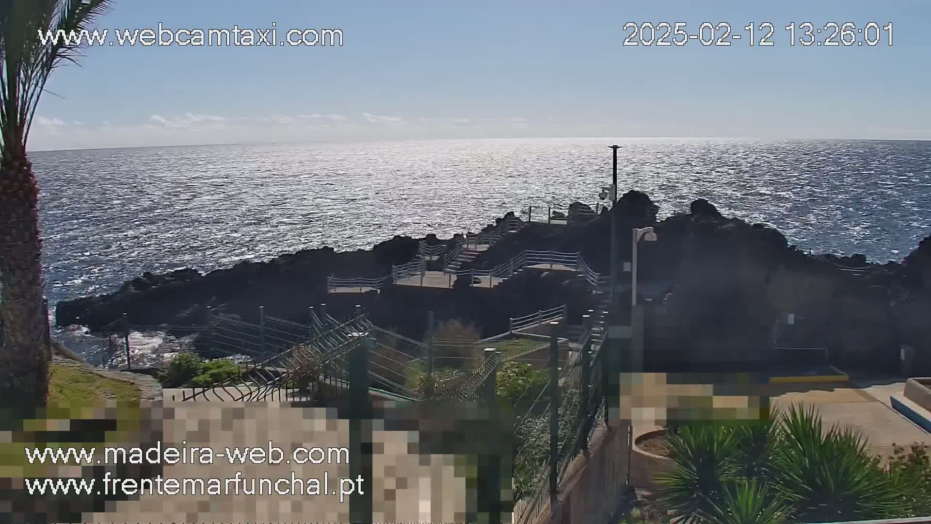 A rocky coast with a stairway leading down to the ocean, under a mostly sunny sky.