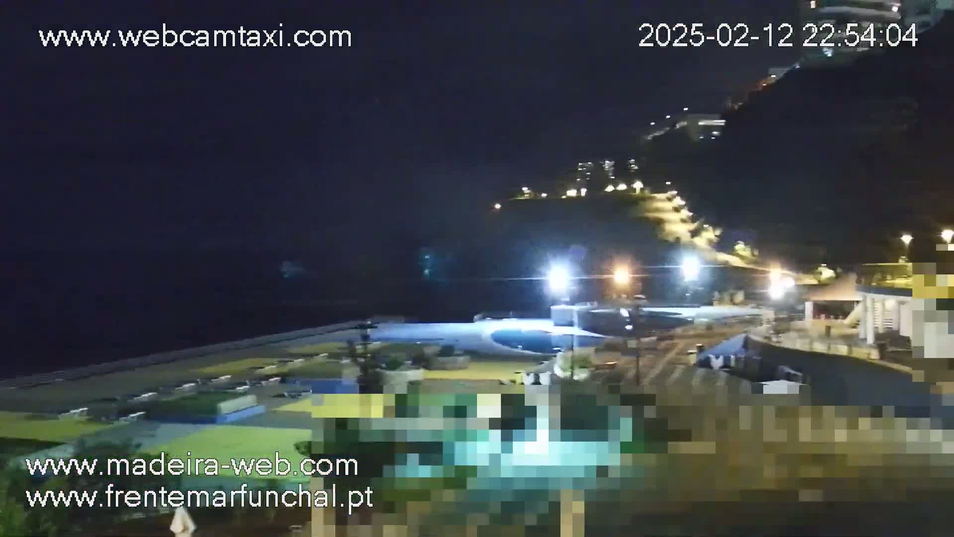 A nighttime view of a coastal area with buildings and a pool illuminated, under a clear, dark sky.