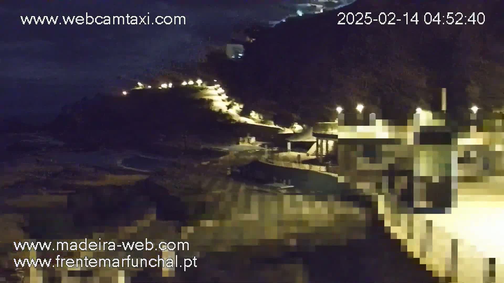 A nighttime coastal scene shows a dark, hilly area with a path illuminated by lights leading to a building near the water's edge.