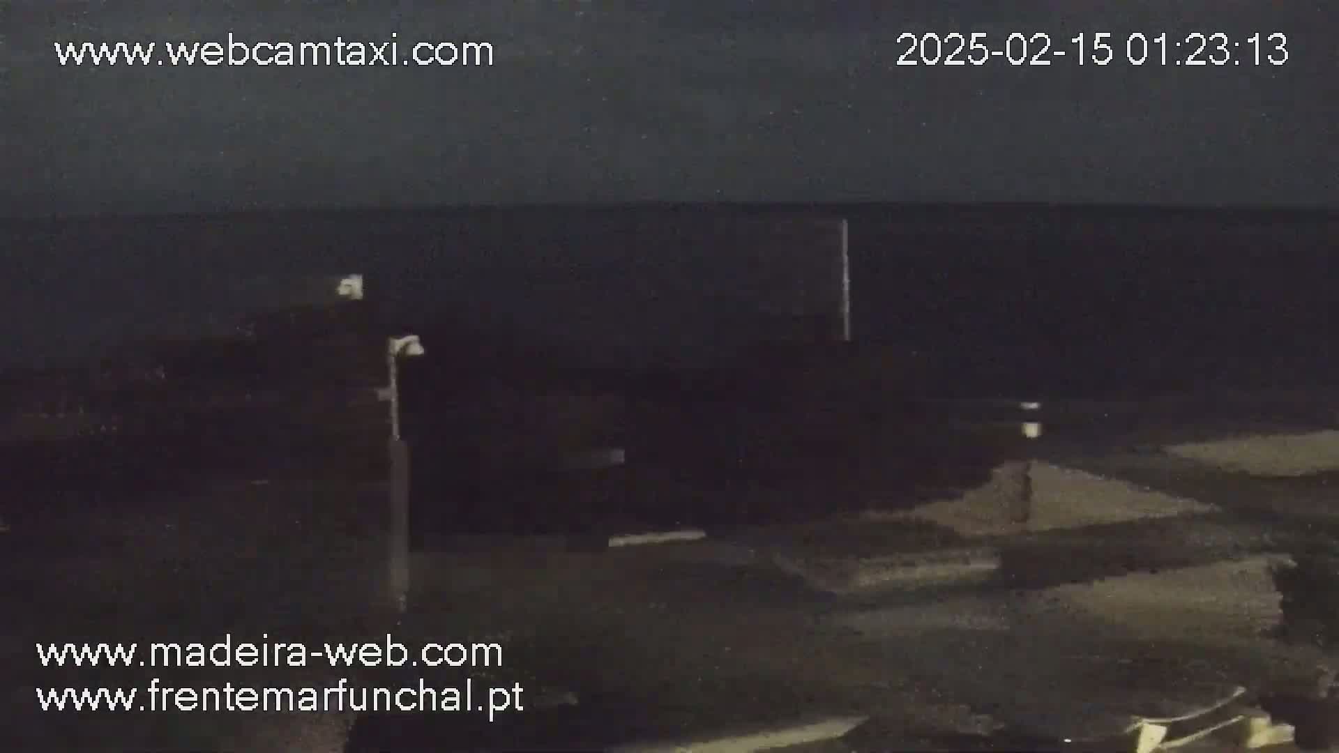 A nighttime, dark view of a mostly empty street near a body of dark water under a dark sky.