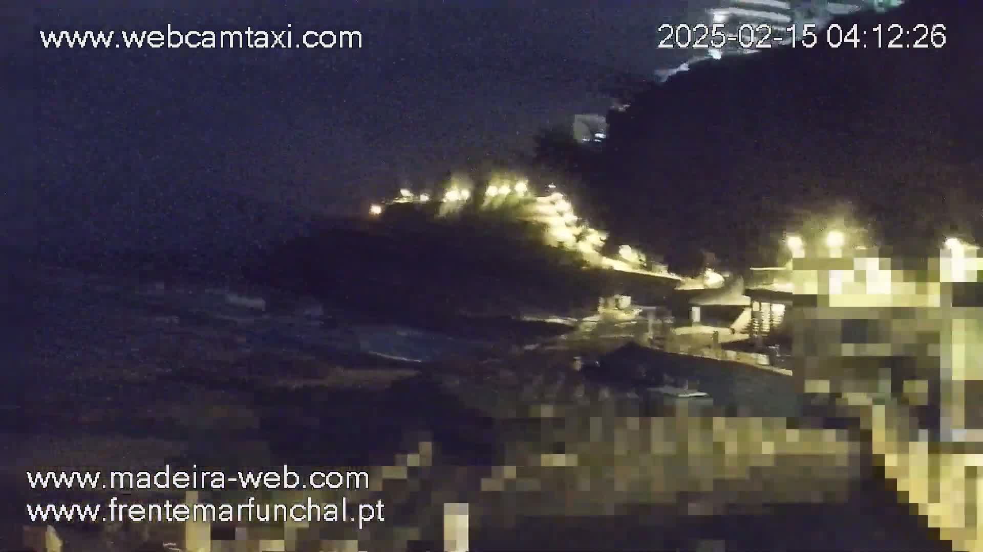 A nighttime view of a dark, wavy ocean near a dimly lit shoreline with buildings and lights on a hill.