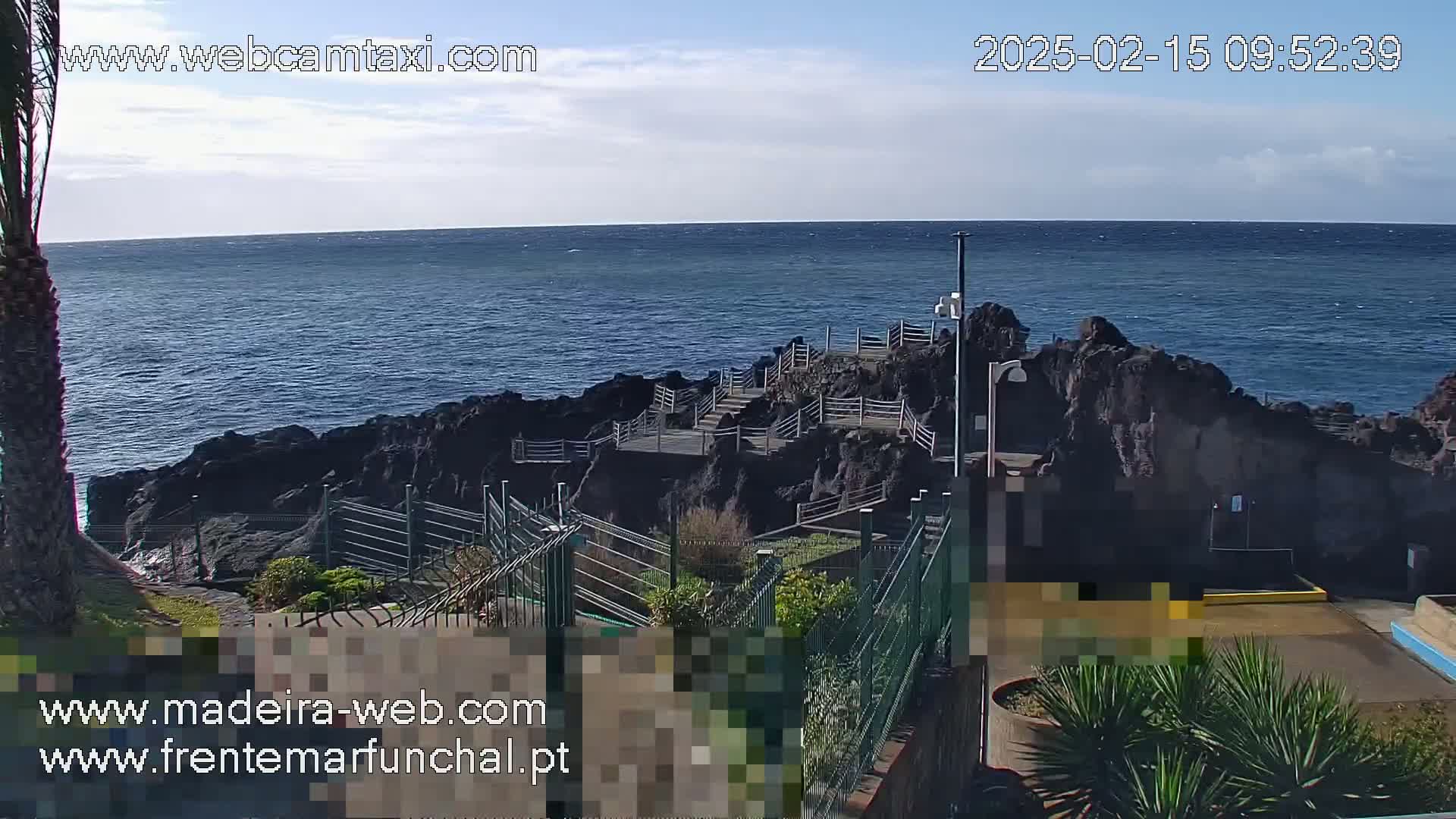 A rocky coastline with a stairway leading down to the ocean under mostly clear skies.