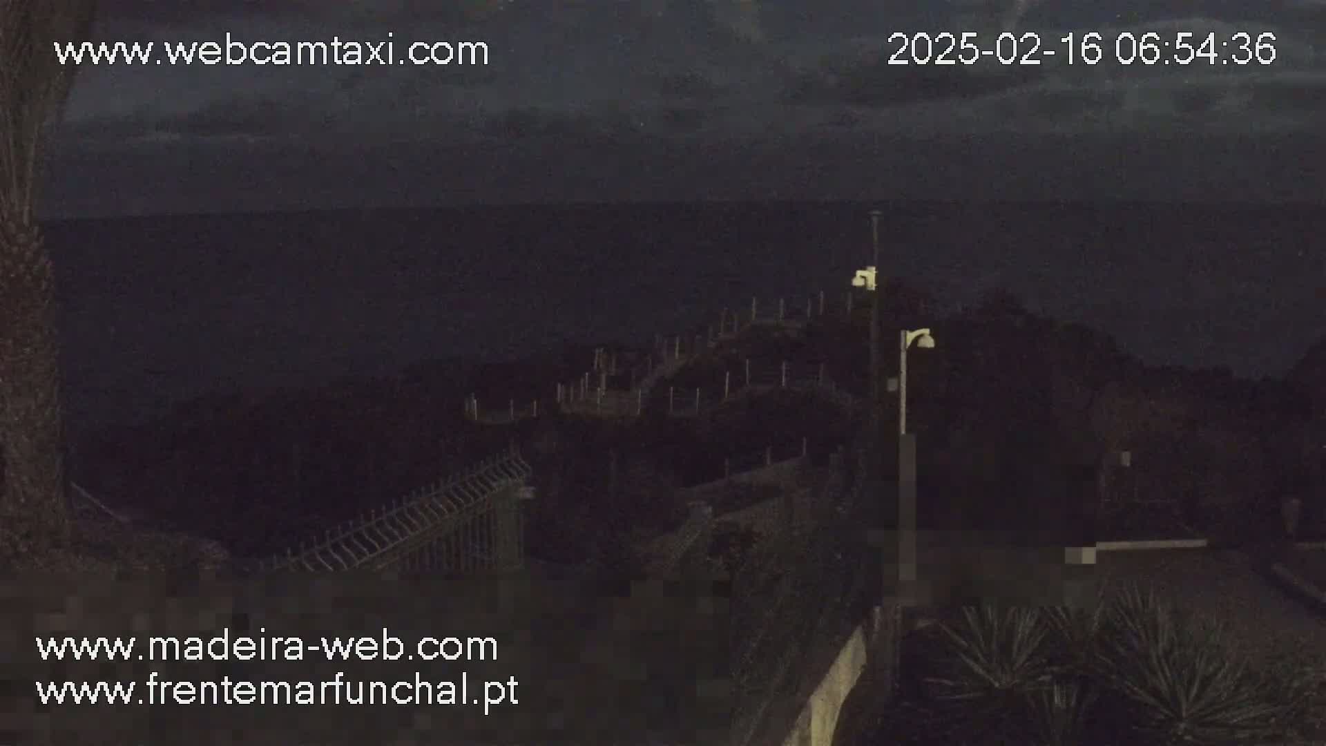 A dark, nighttime coastal scene shows a stairway leading down to the ocean under a cloudy sky.