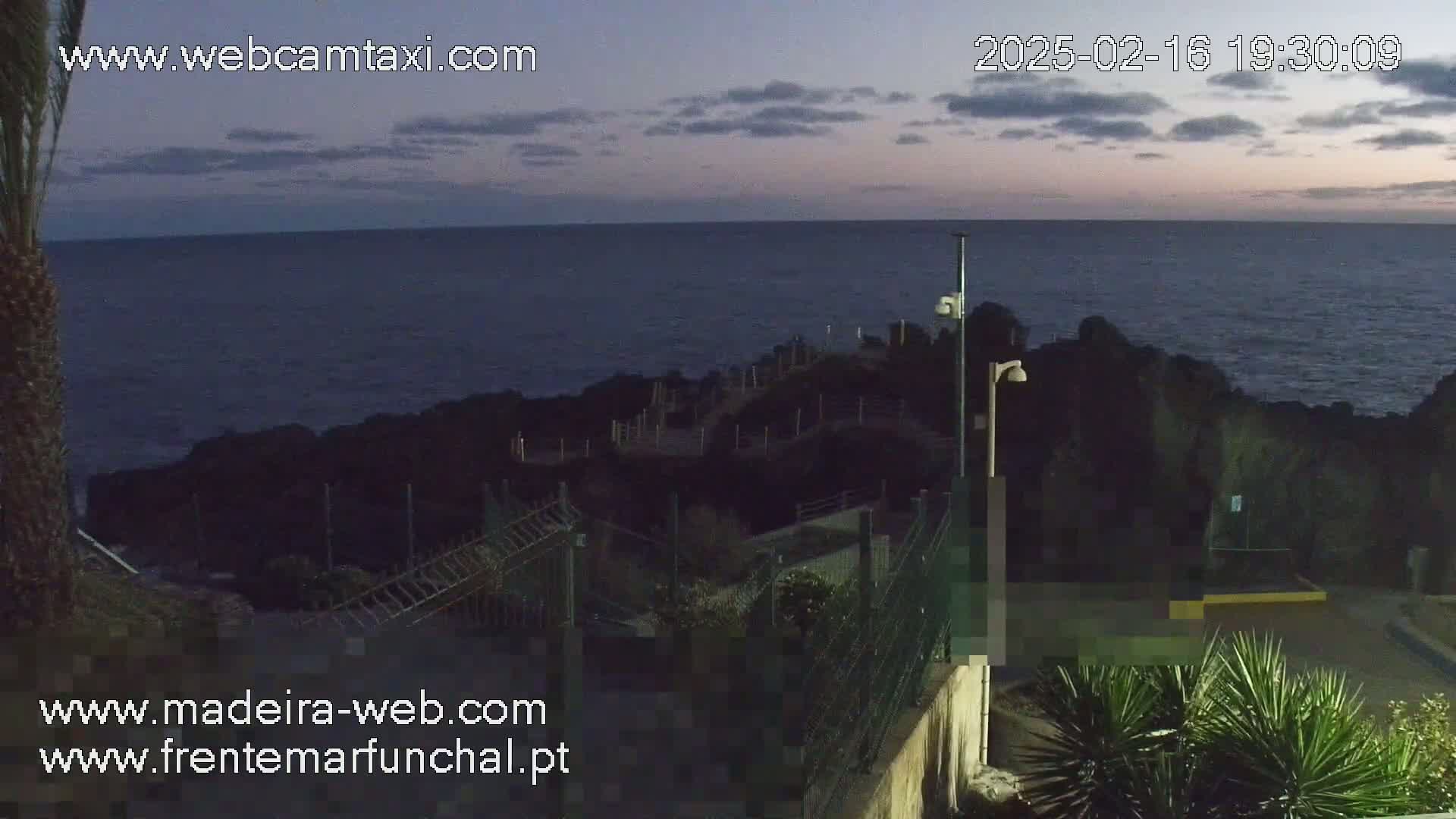A dark, calm ocean is visible at dusk from a coastal viewpoint with a pathway and fencing.