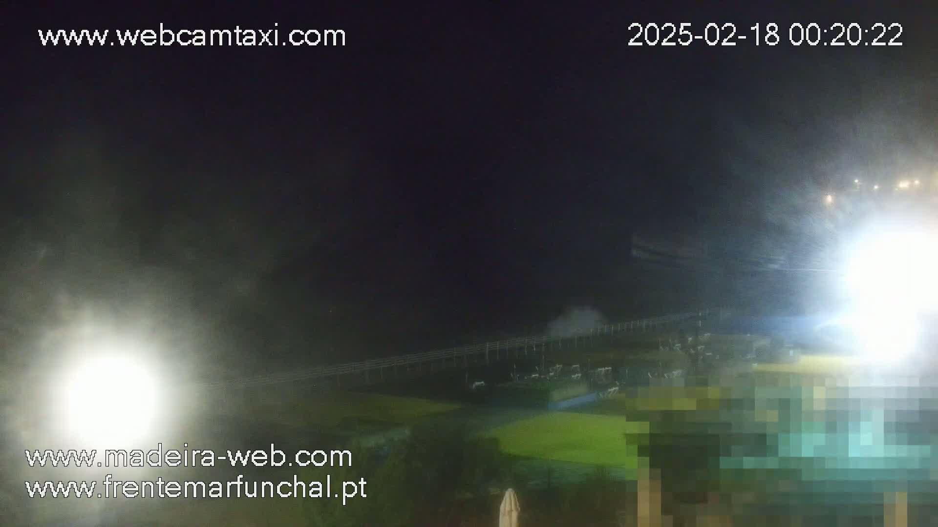 A nighttime, blurry view of a waterfront area with bright lights and what appears to be mist or spray in the air.
