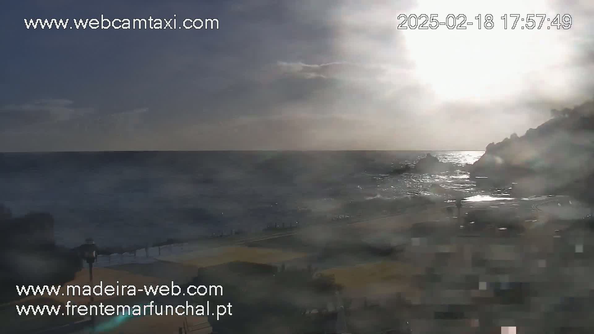 A partly cloudy day shows a rocky coastline with a somewhat choppy sea under a hazy sun.