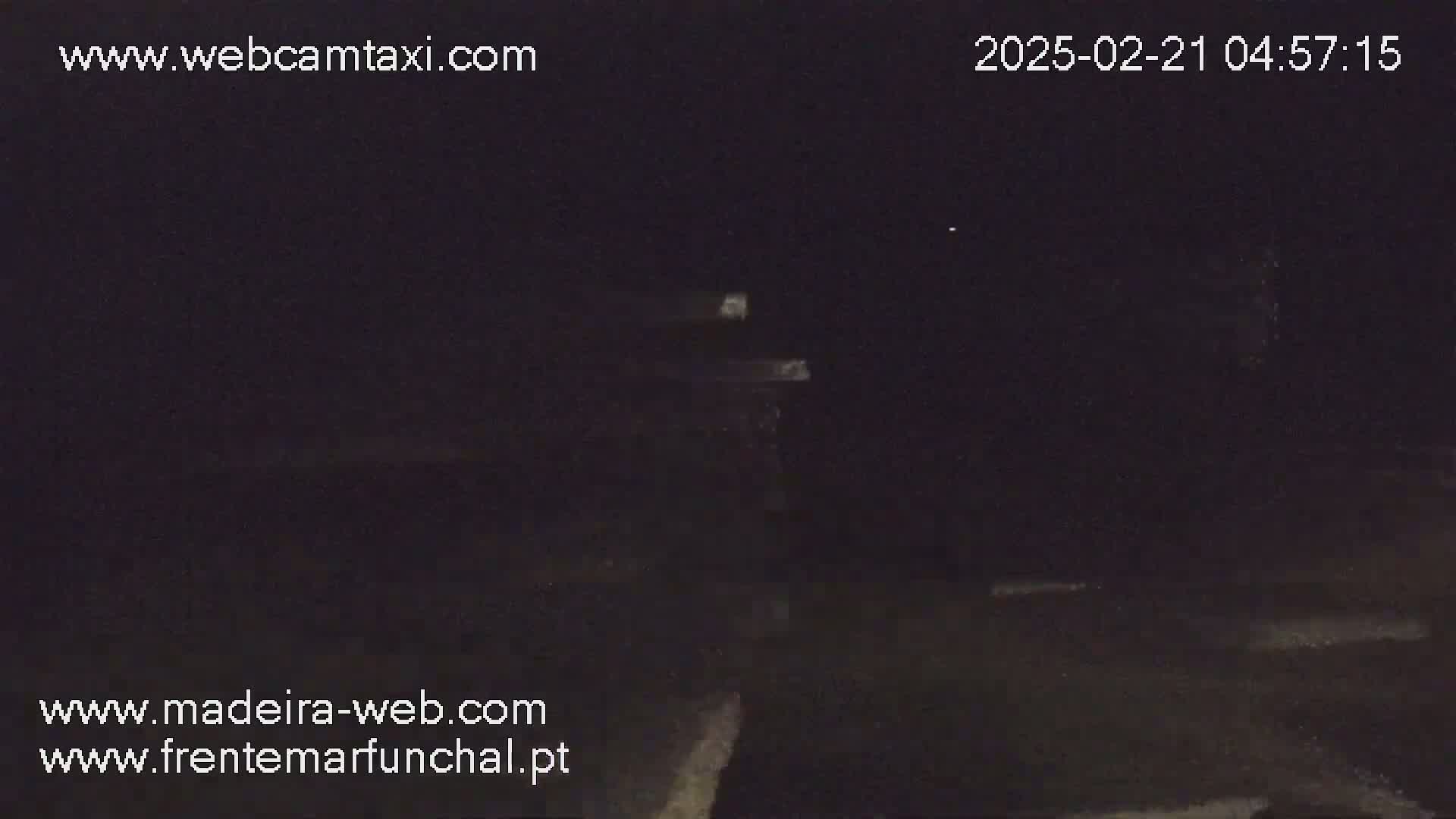 A dark, nighttime outdoor scene shows a dimly lit structure or object in the distance.
