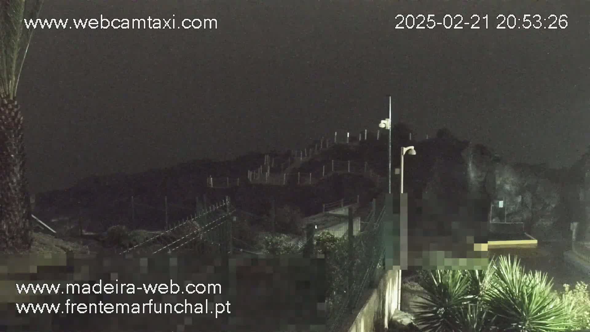 A nighttime outdoor scene shows a dark hill with a fence and some vegetation at the bottom, under a dark, cloudy sky.