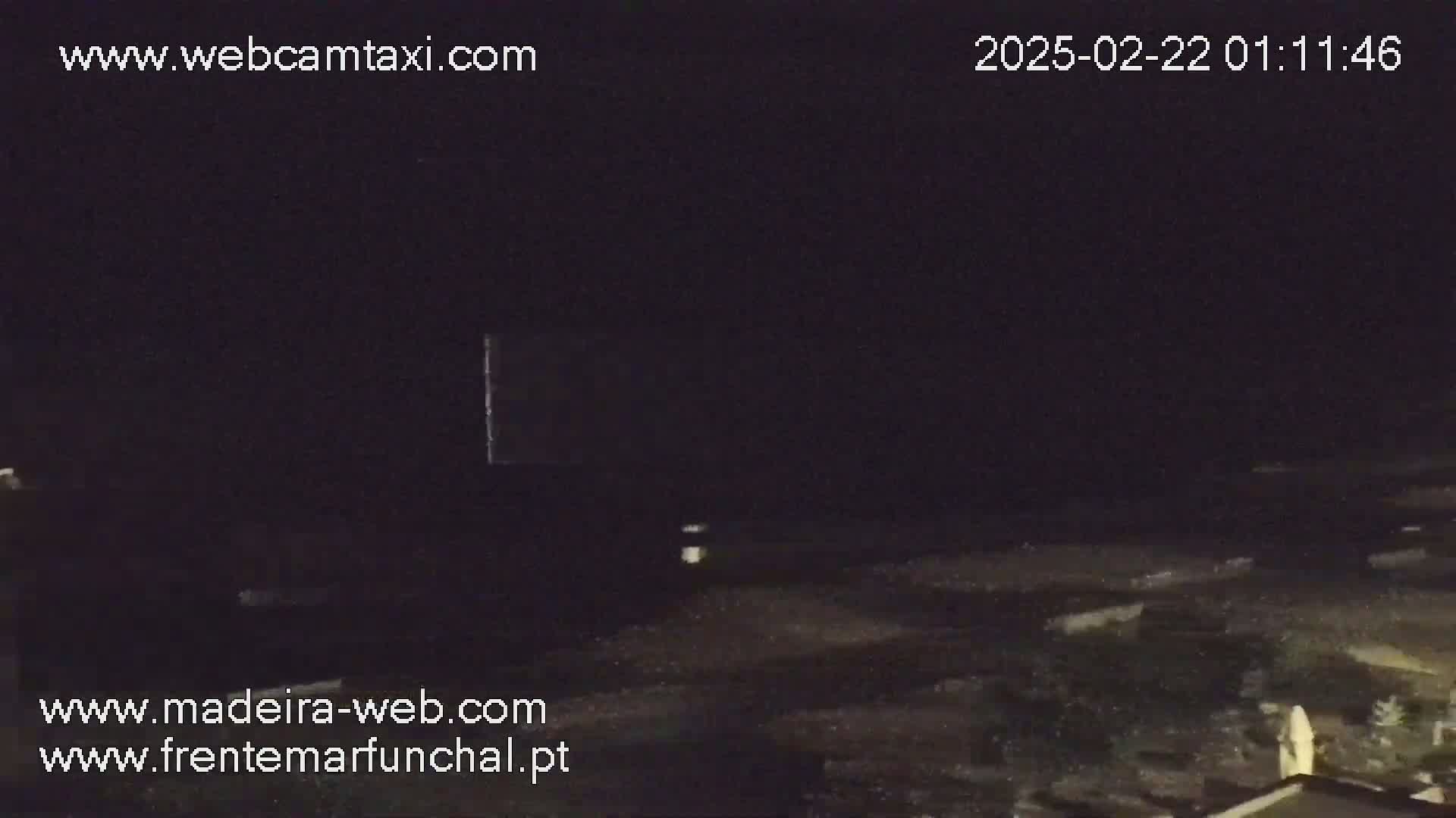 A dark, nighttime outdoor scene shows a mostly empty expanse of ground with a few indistinct objects visible under a completely dark sky.