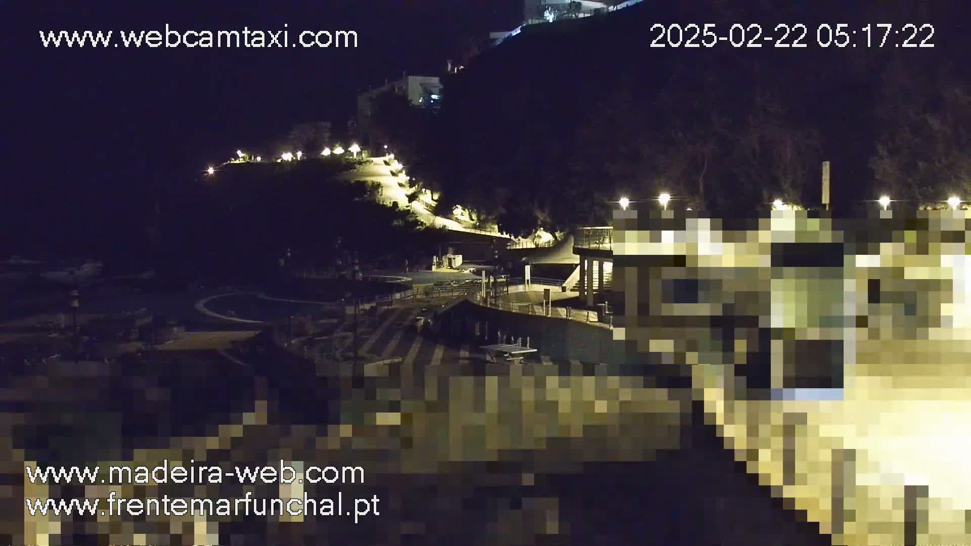 A nighttime, outdoor view of a coastal area with a building illuminated by lights, a winding path leading up a hillside, and a parking area.